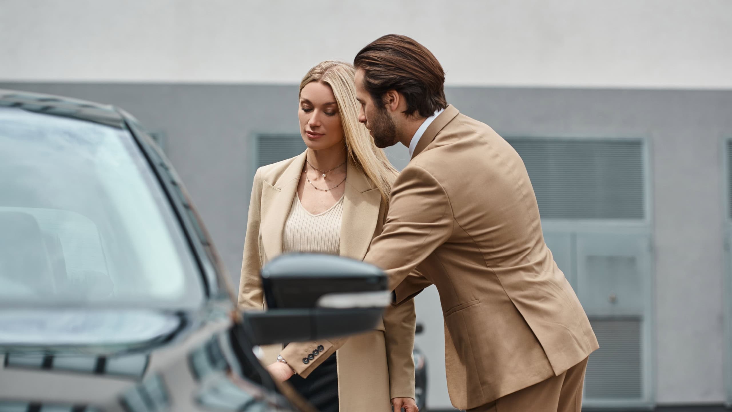 elegant bearded man opening rear door of luxury car near stylish blonde businesswoman on street