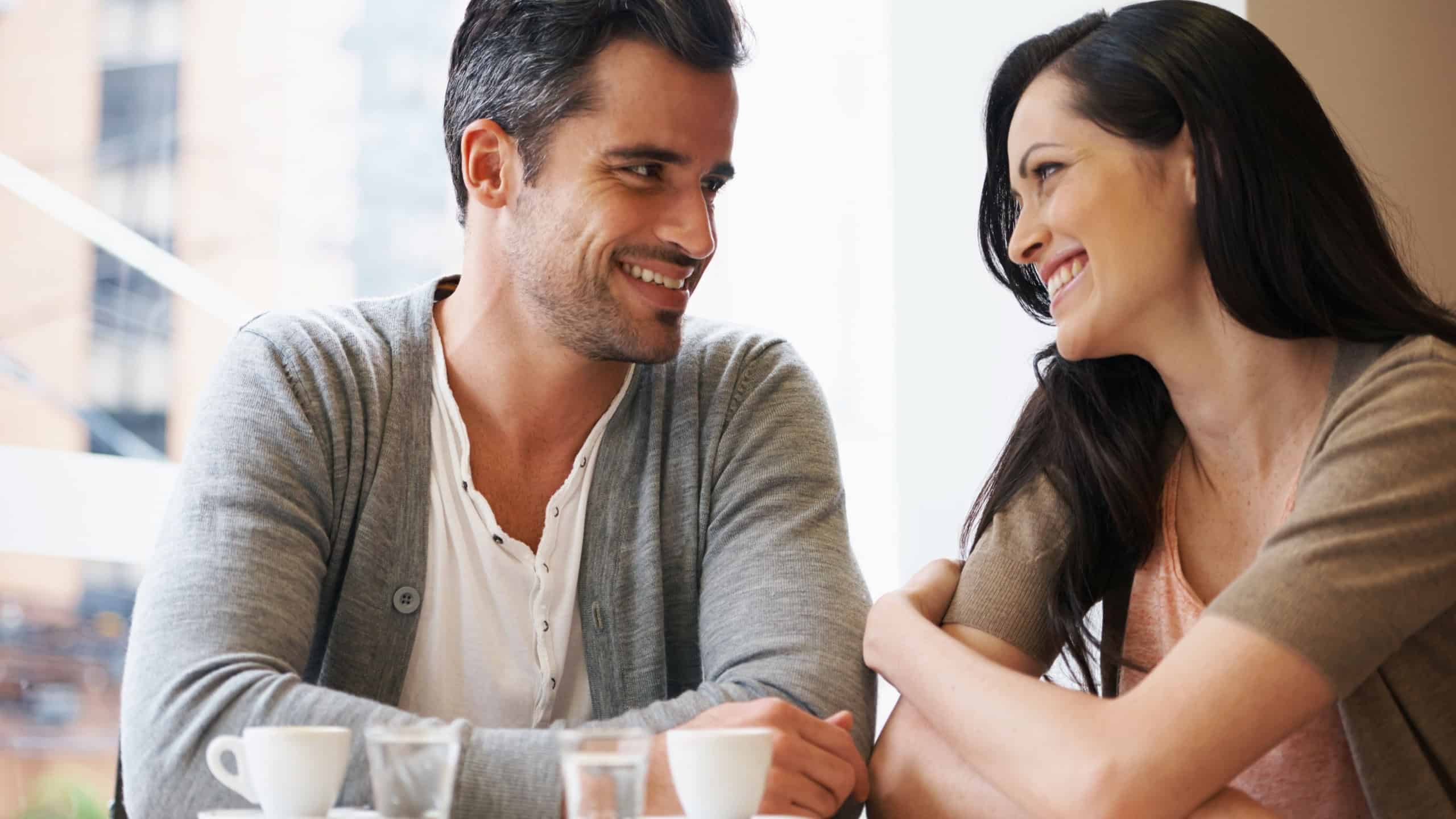 Love, talking and couple with coffee on date for romance or anniversary in cafeteria. Happy, bonding and young man and woman in conversation drinking latte, espresso or cappuccino at restaurant.
