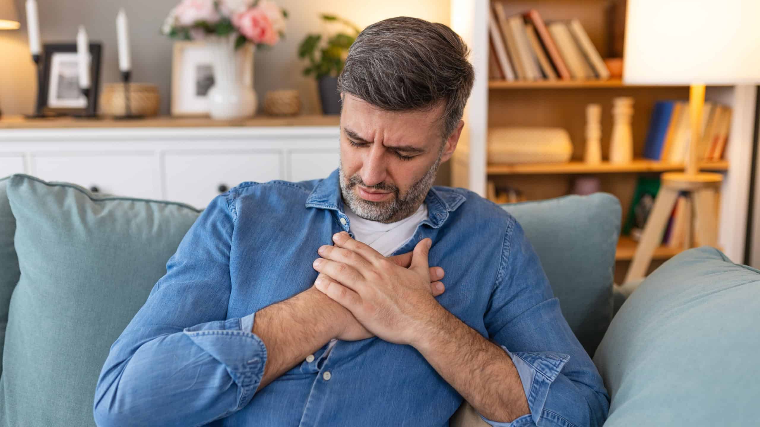 Man presses hand to chest has heart attack suffers from unbearable pain, Mature man with pain on heart in living room. man suffering from bad pain in his chest heart attack at home