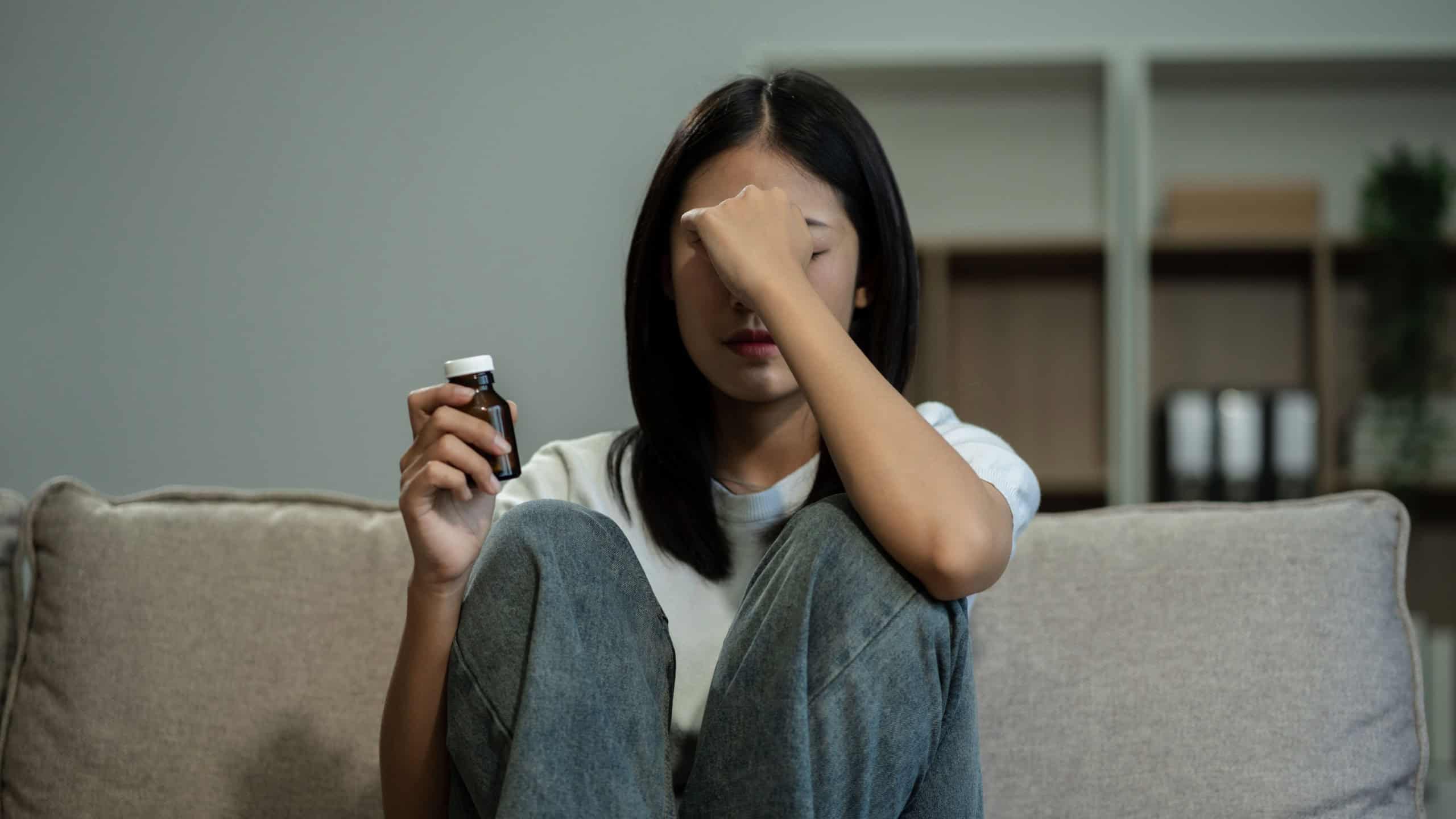 Depressed woman holding a glass of water, suffering from headaches, fighting stress with antidepressants, close-up view.