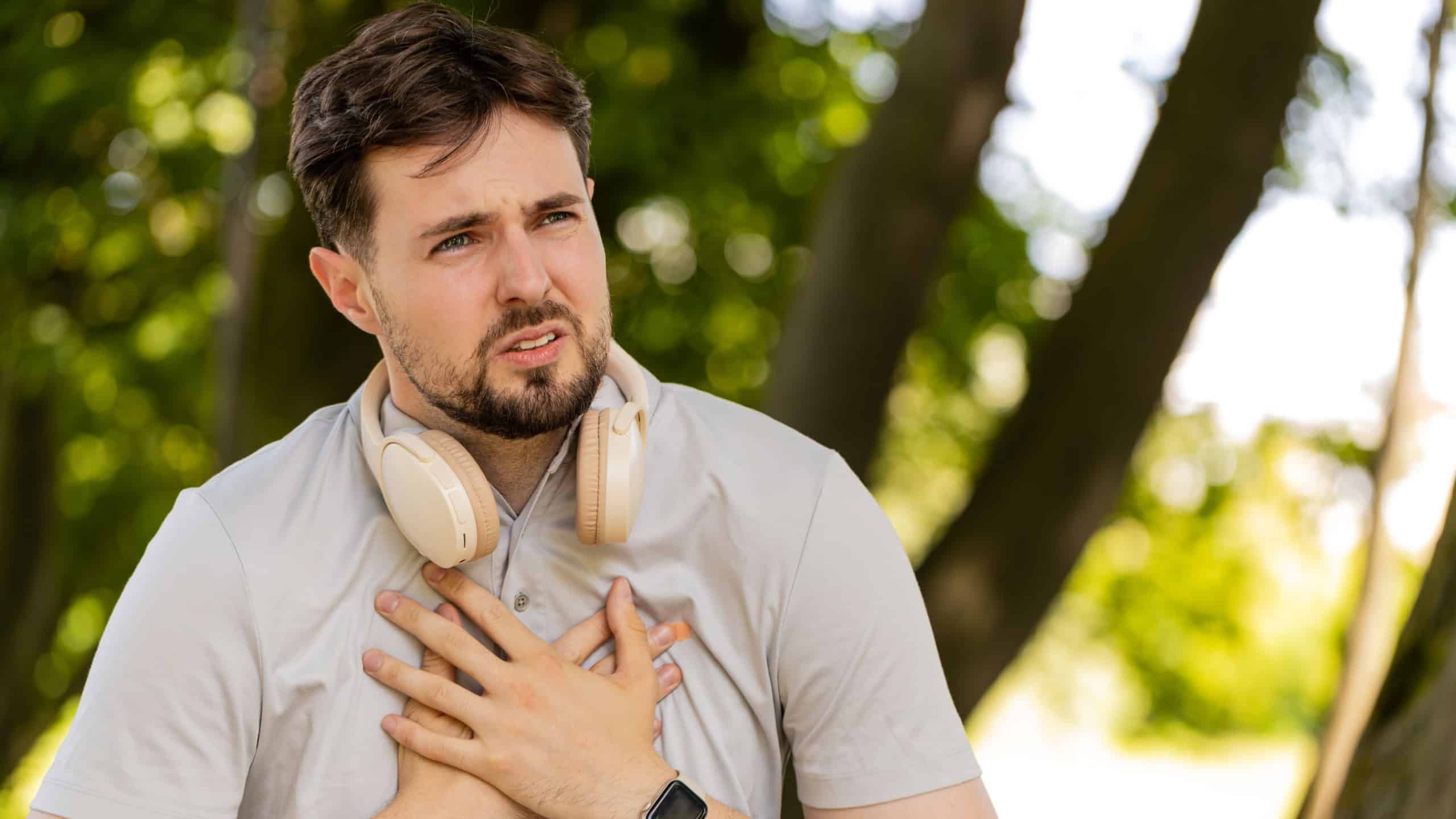 Young adult sports man runner jogger having heart attack or chest pain after running workout in urban city park. A tired athlete suffers from tension in the heart. Health care and sports concept.