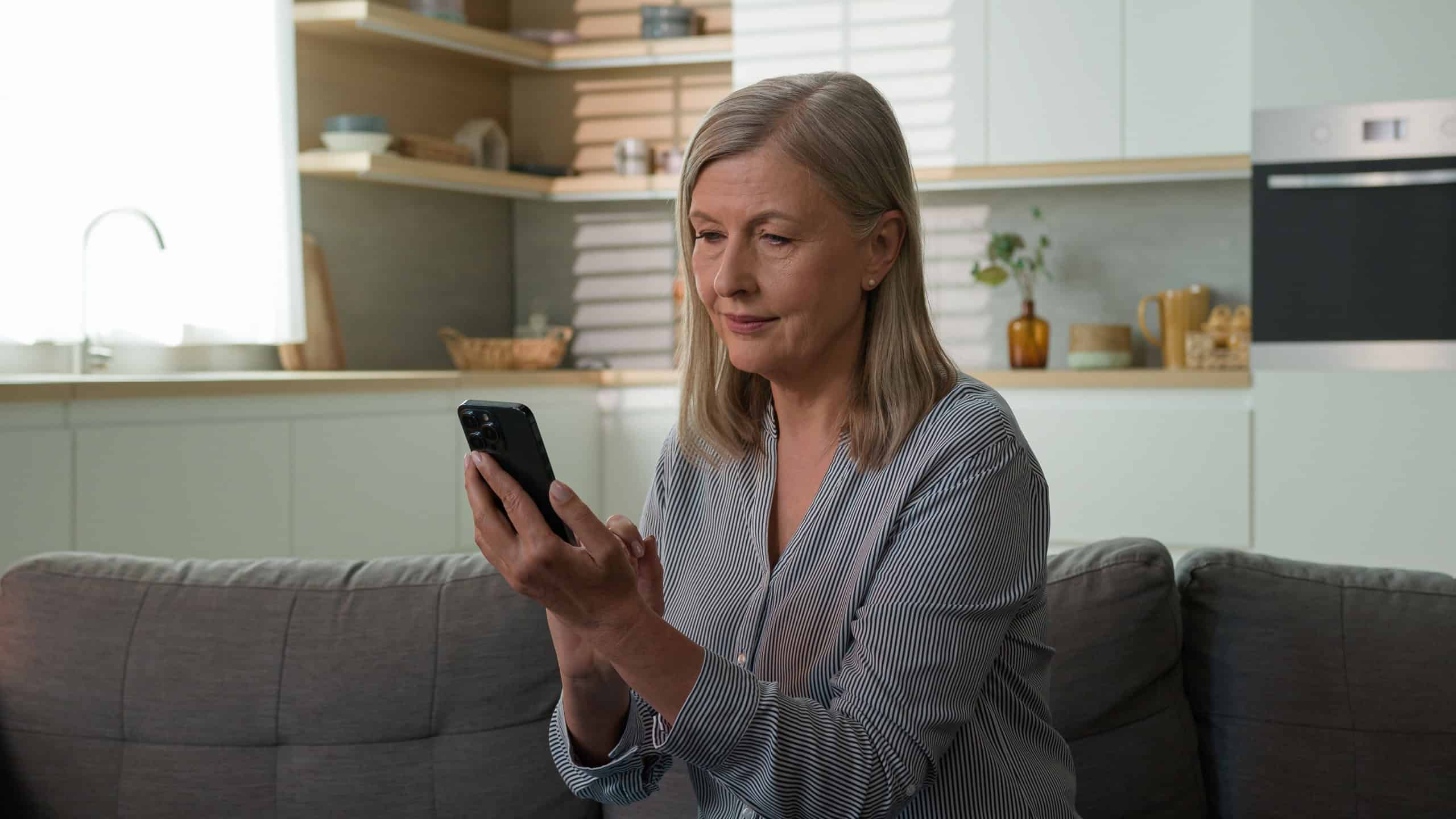 Smiling senior mature Caucasian woman elderly grandparent scrolling screen typing mobile phone choose clothes in online shop mother pensioner old female browsing Internet use banking app at home couch