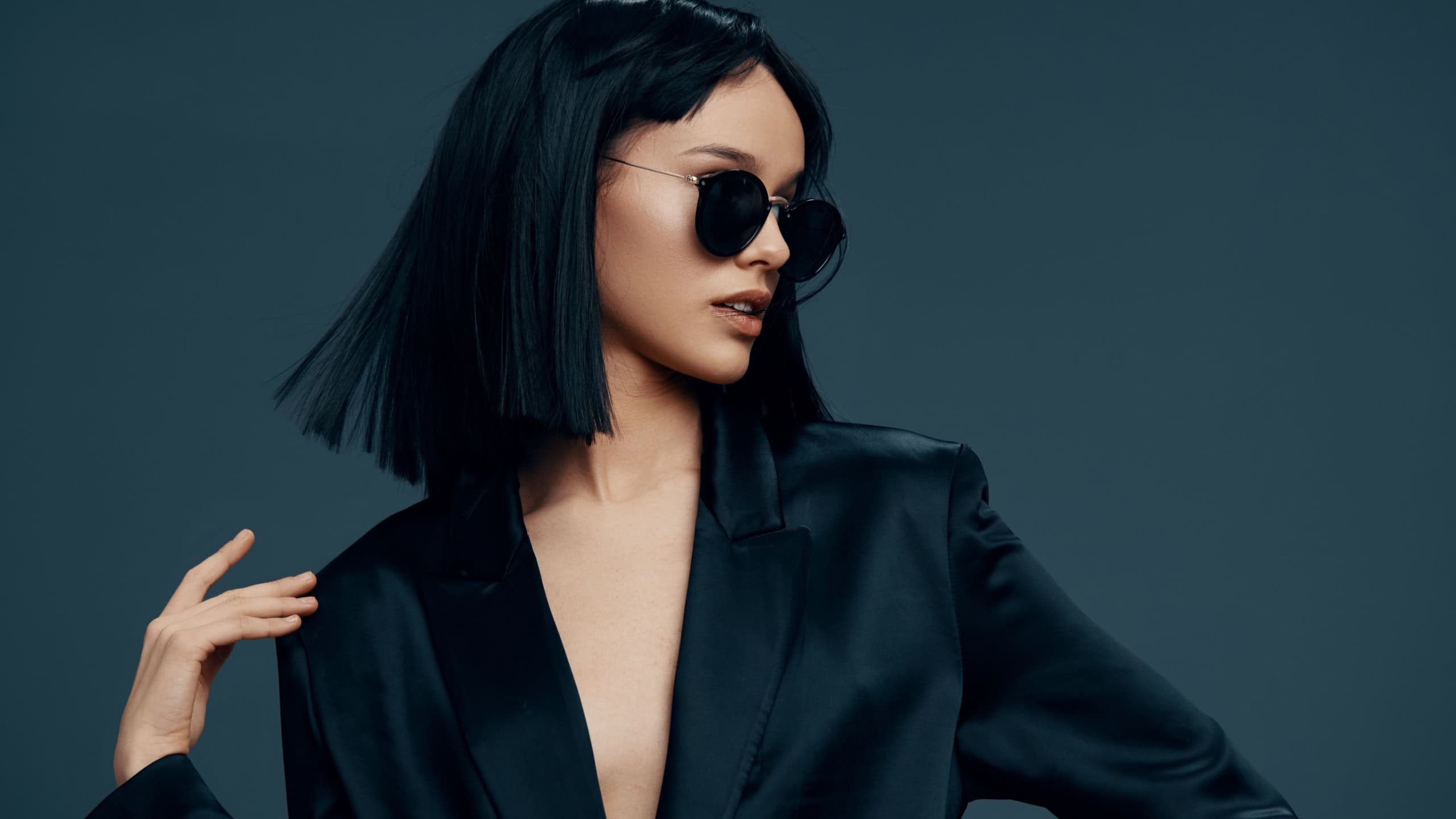 Asian woman in black suit and sunglasses on a dark background, exuding confidence and elegance, showcasing contemporary fashion with a sophisticated and mysterious vibe