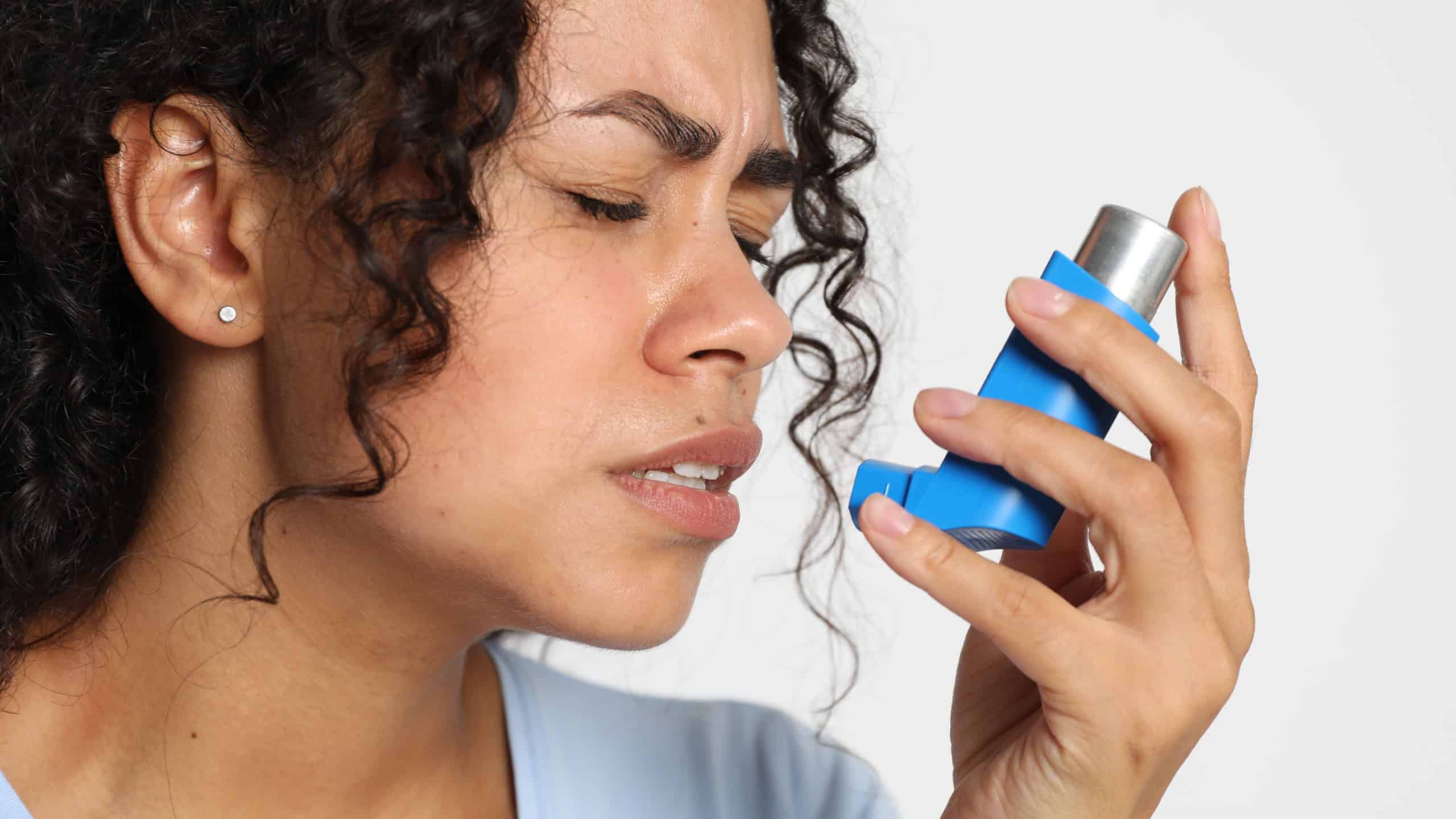 Young woman using asthma inhaler on white background, closeup