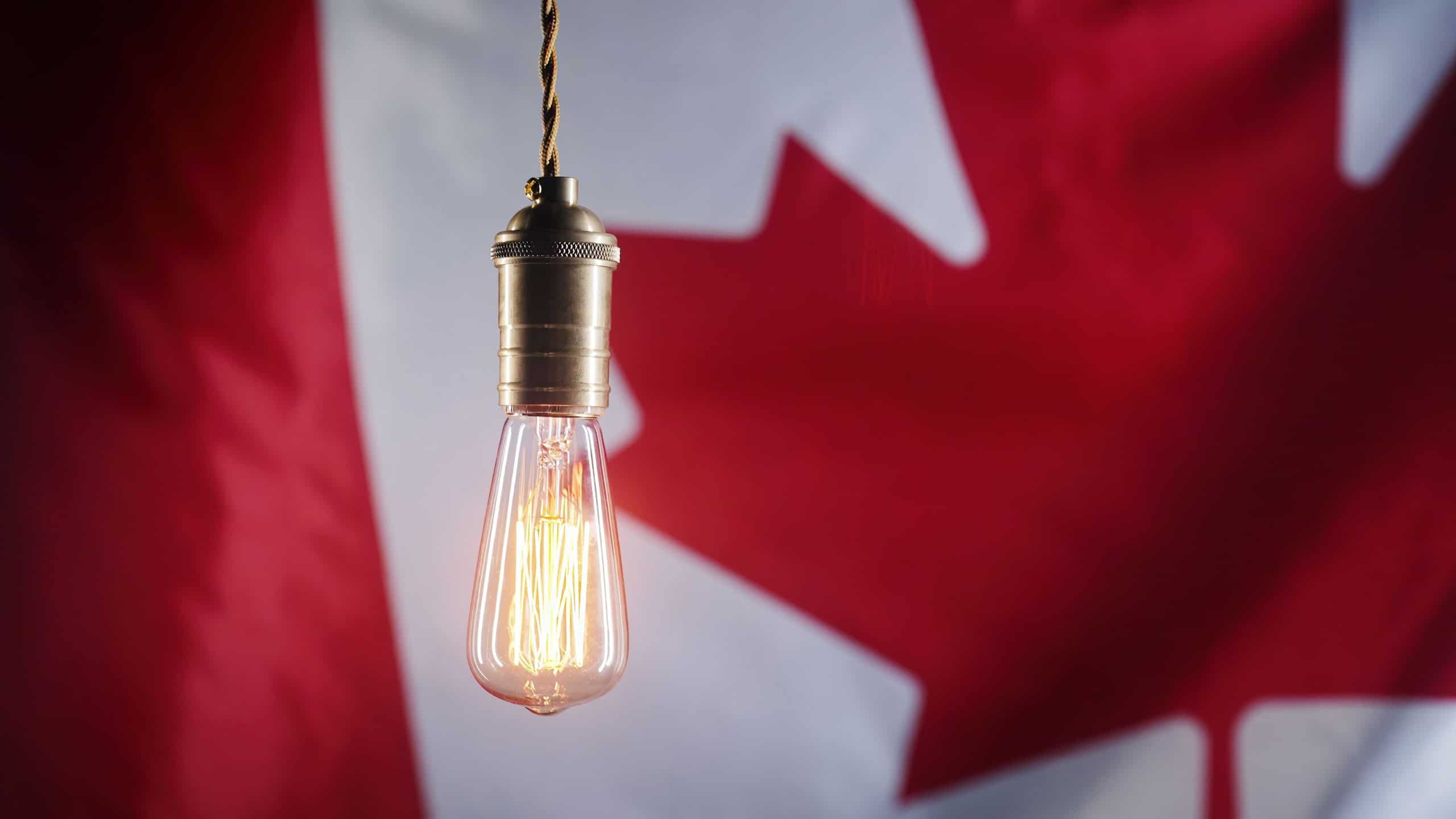 Flickering classic antique Edison Tungsten filament lamp on waving canadian flag background. Raising tariffs for electricity supply, bills, energy crisis in Canada. High quality