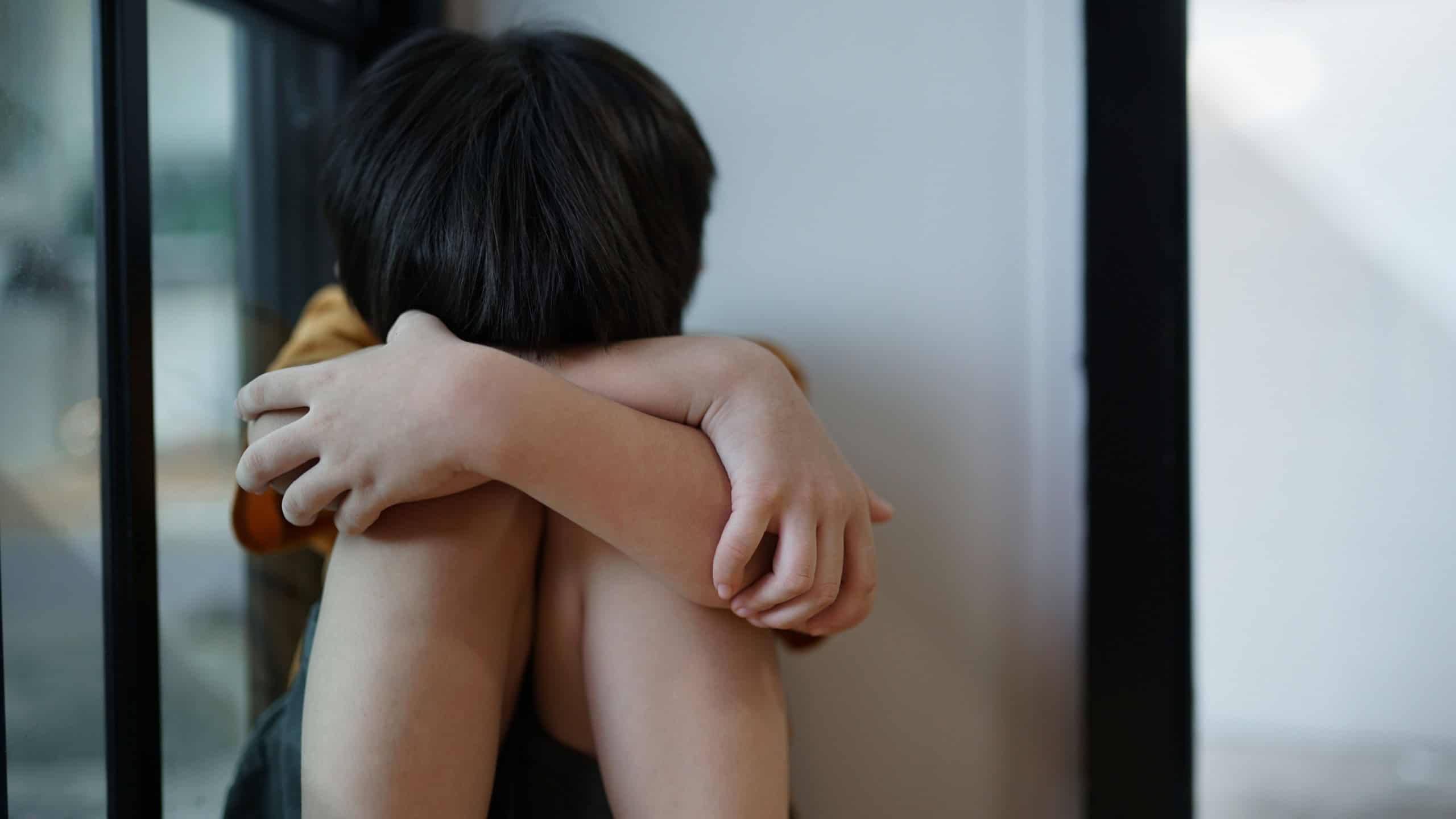 A sad young boy sat in the corner crying and covering her face with her hands. The concept of child abuse in the family Parents punish their children into a corner, the child is depressed, crying, lif