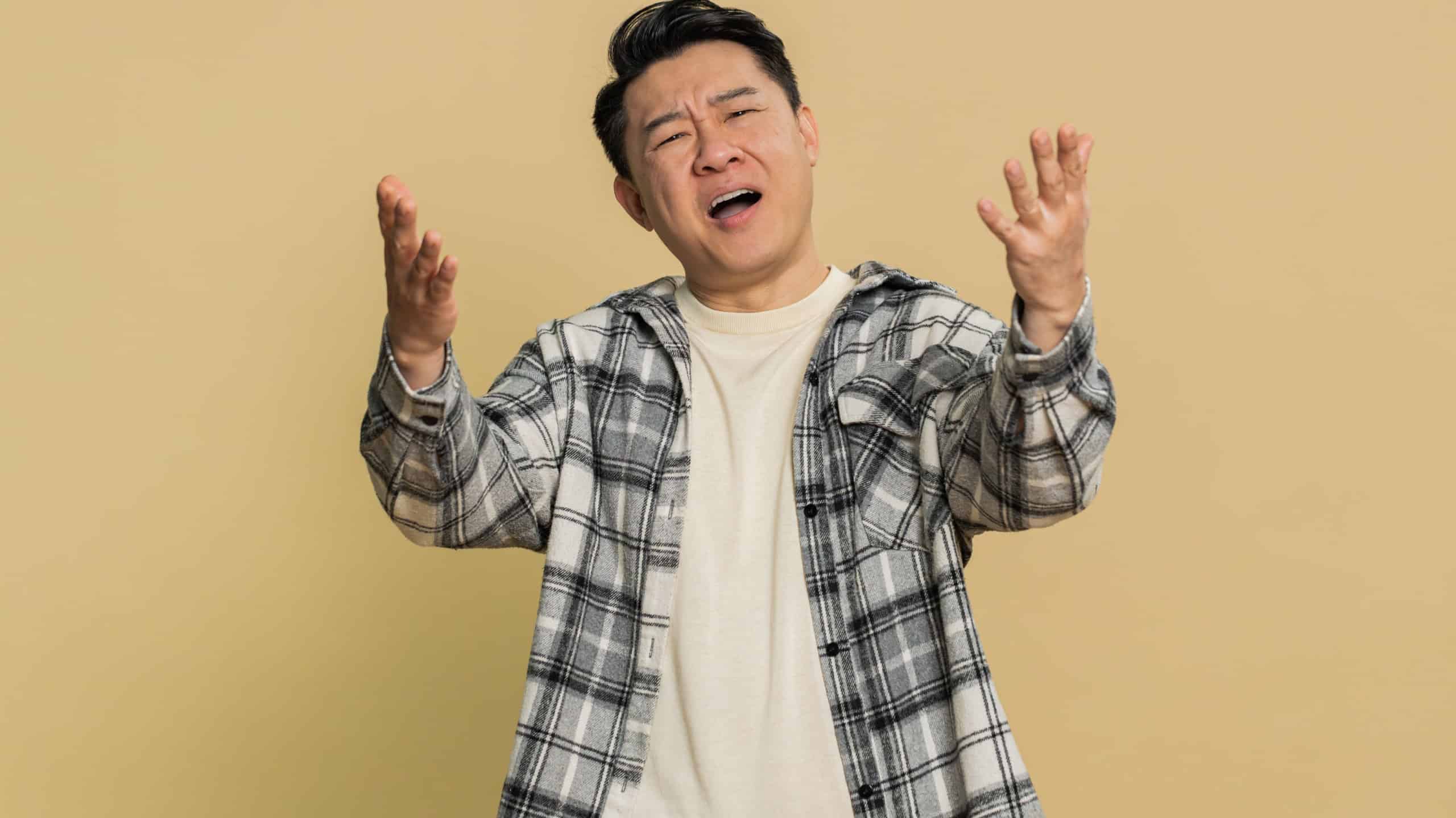 Sad young Asian man feeling hopelessness loneliness, nervous breakdown, loses becoming surprised by lottery results, bad fortune, loss unlucky news. Attractive Chinese guy isolated on beige background