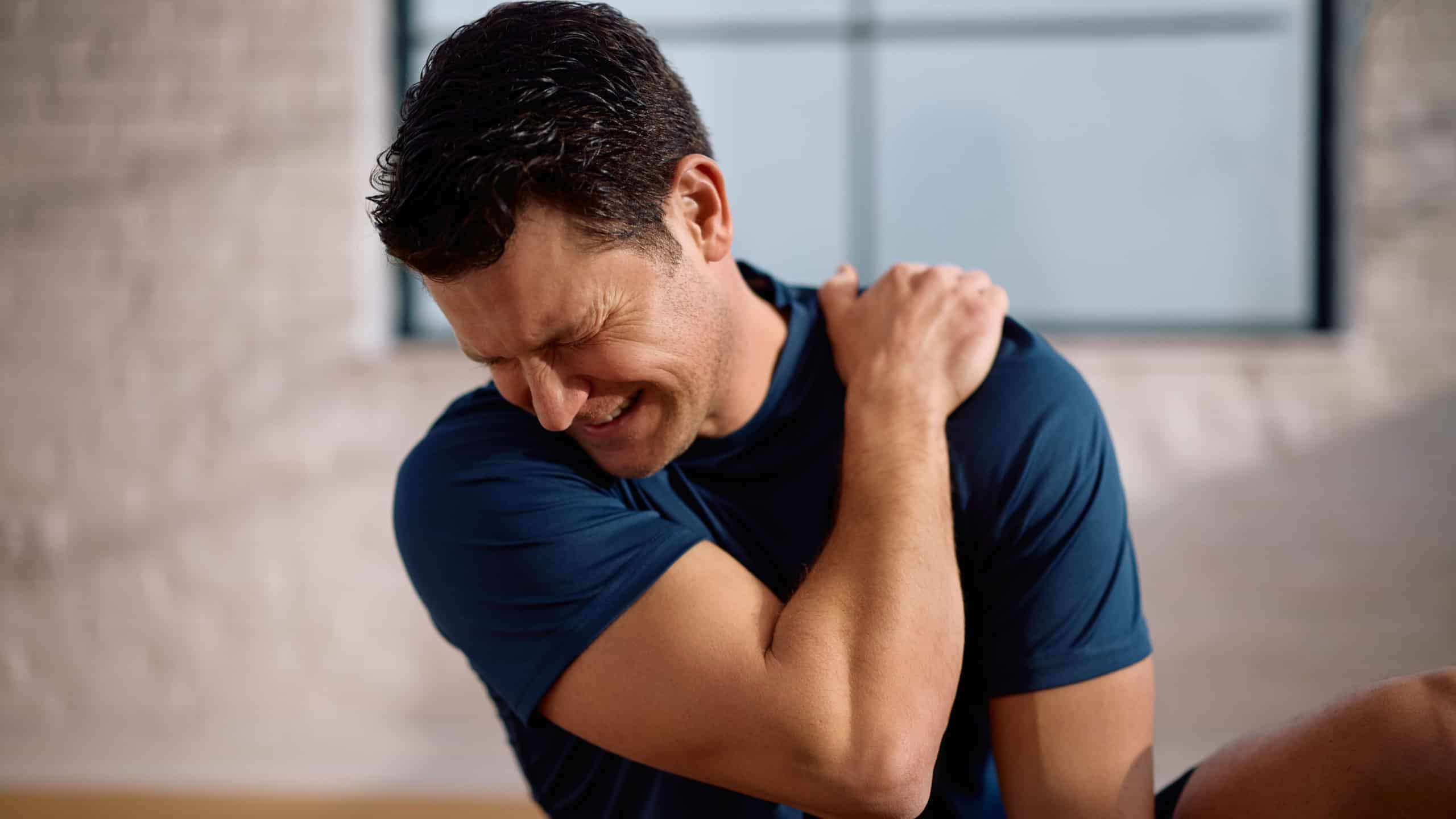 Mid adult sportsman with injured shoulder after exercising at home. 
