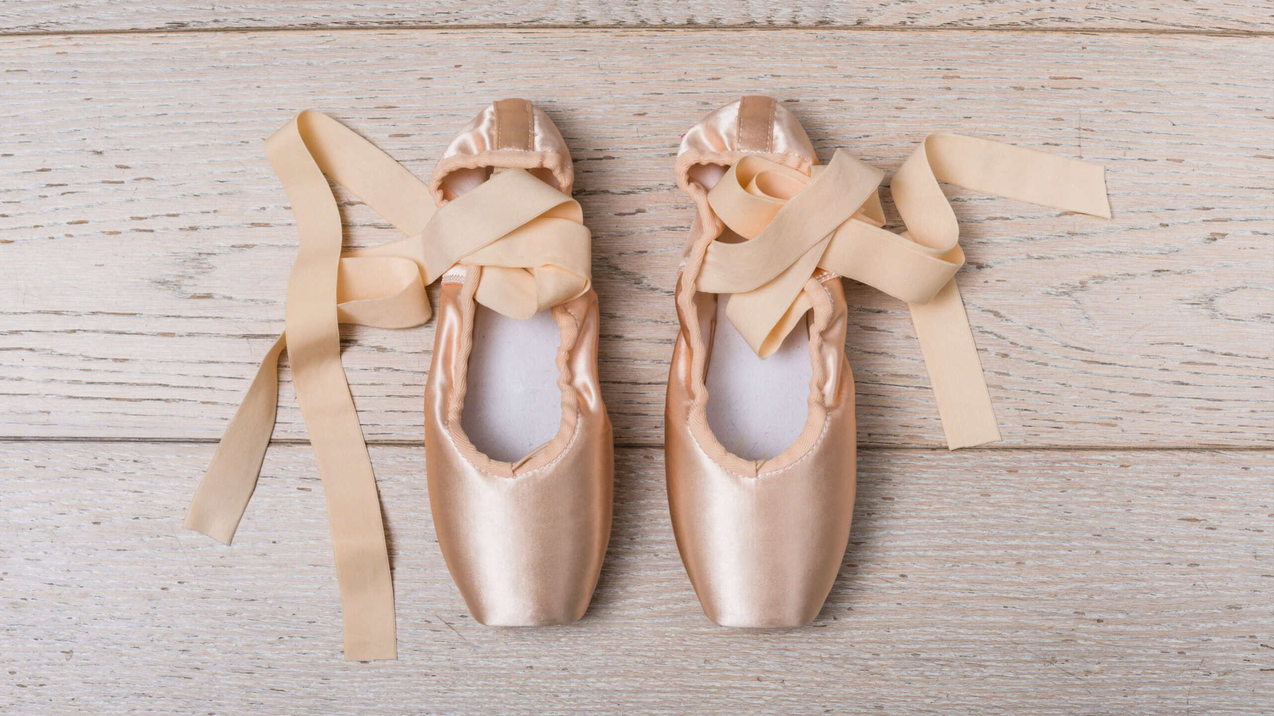 Ballet pointe shoes with satin ribbons lying on wooden floor represent the dedication and grace of classical dance