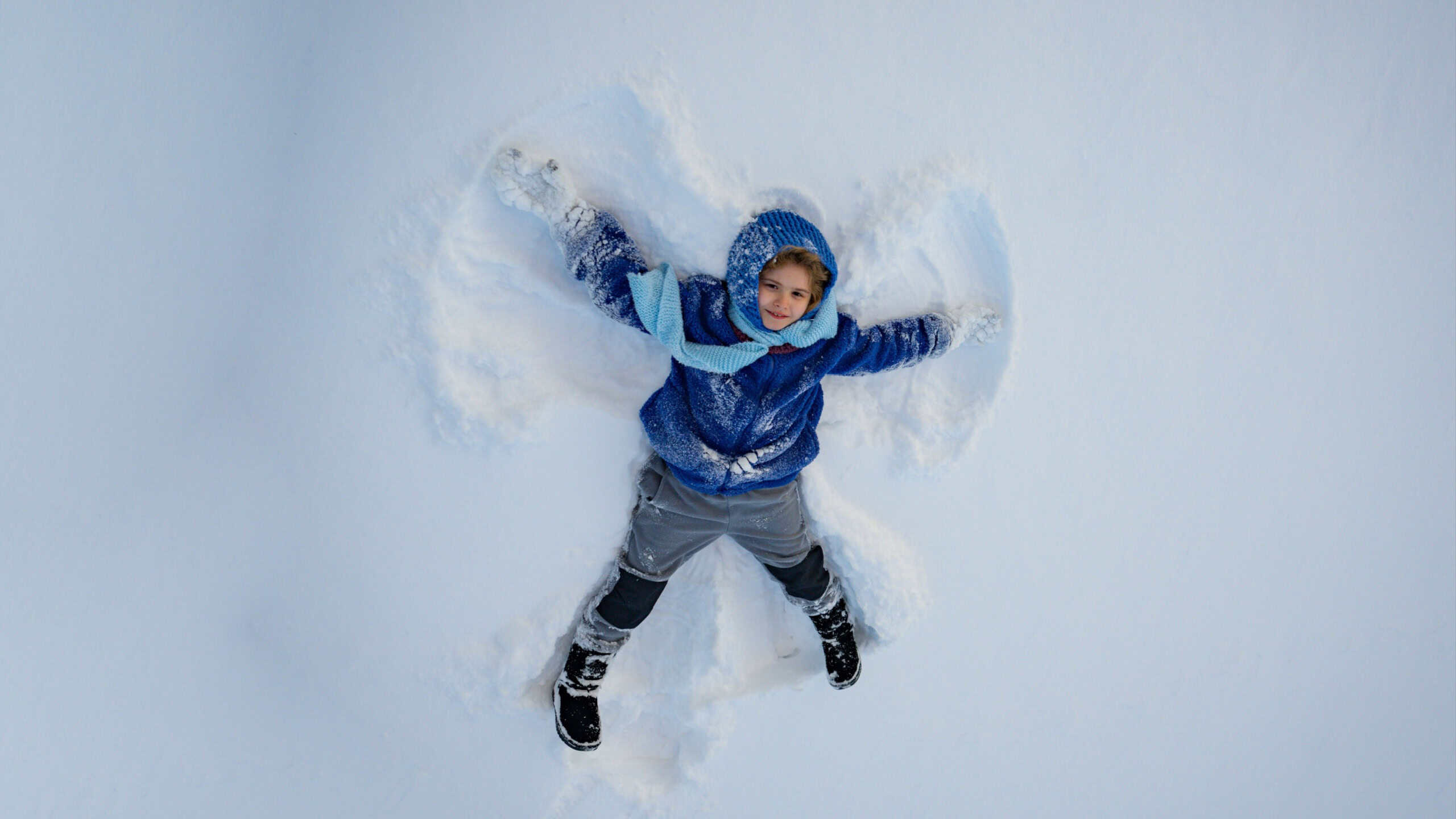 Child making a snow angel. Happy kid lying in the snow. Kid angel in snow. Winter kids with snowy angel wings. Smiling child on a snowy day. Carefree kid in the snow lake angel. Marry Christmas.