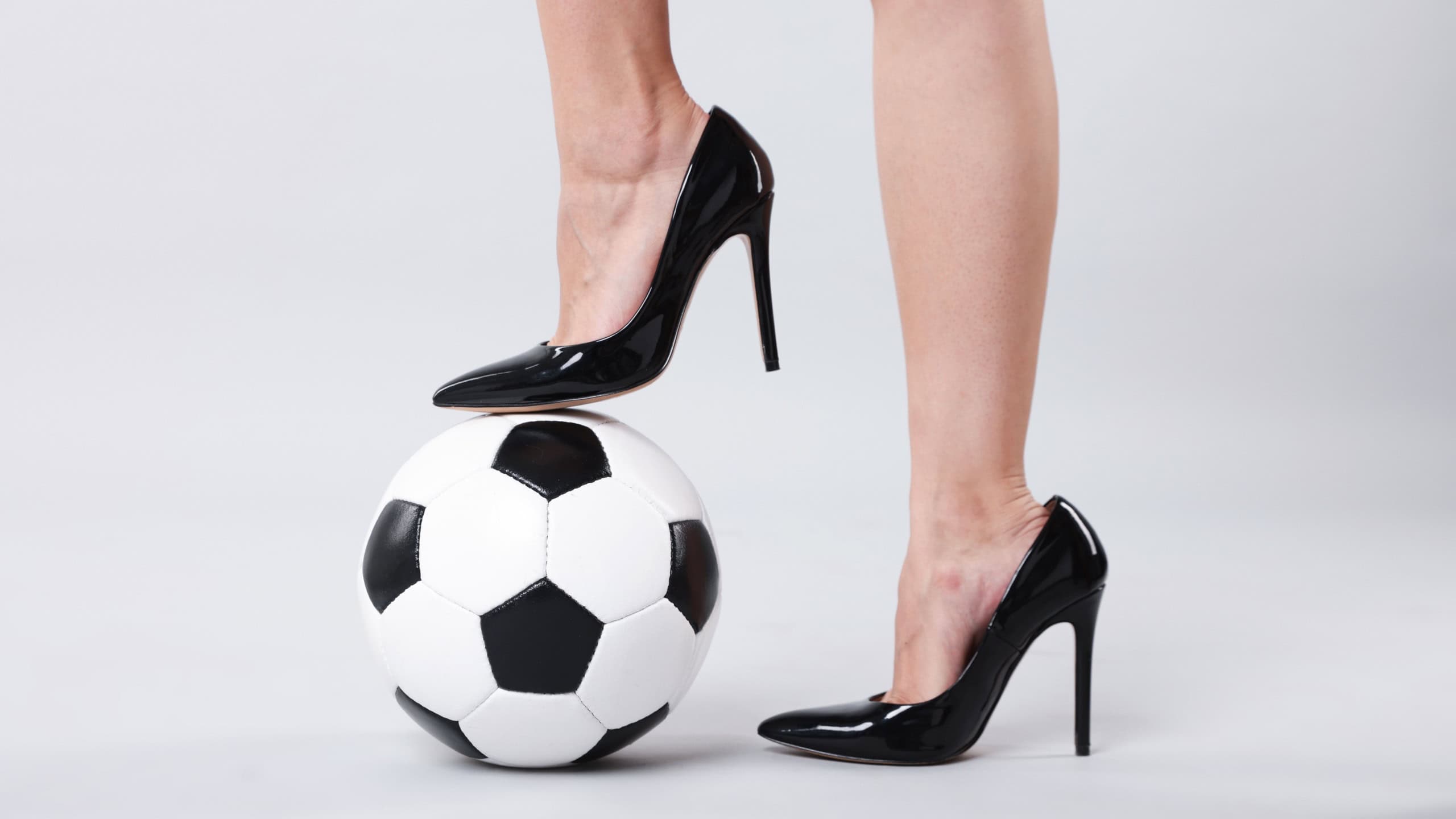 Woman in high heeled shoes with soccer ball on light background, closeup