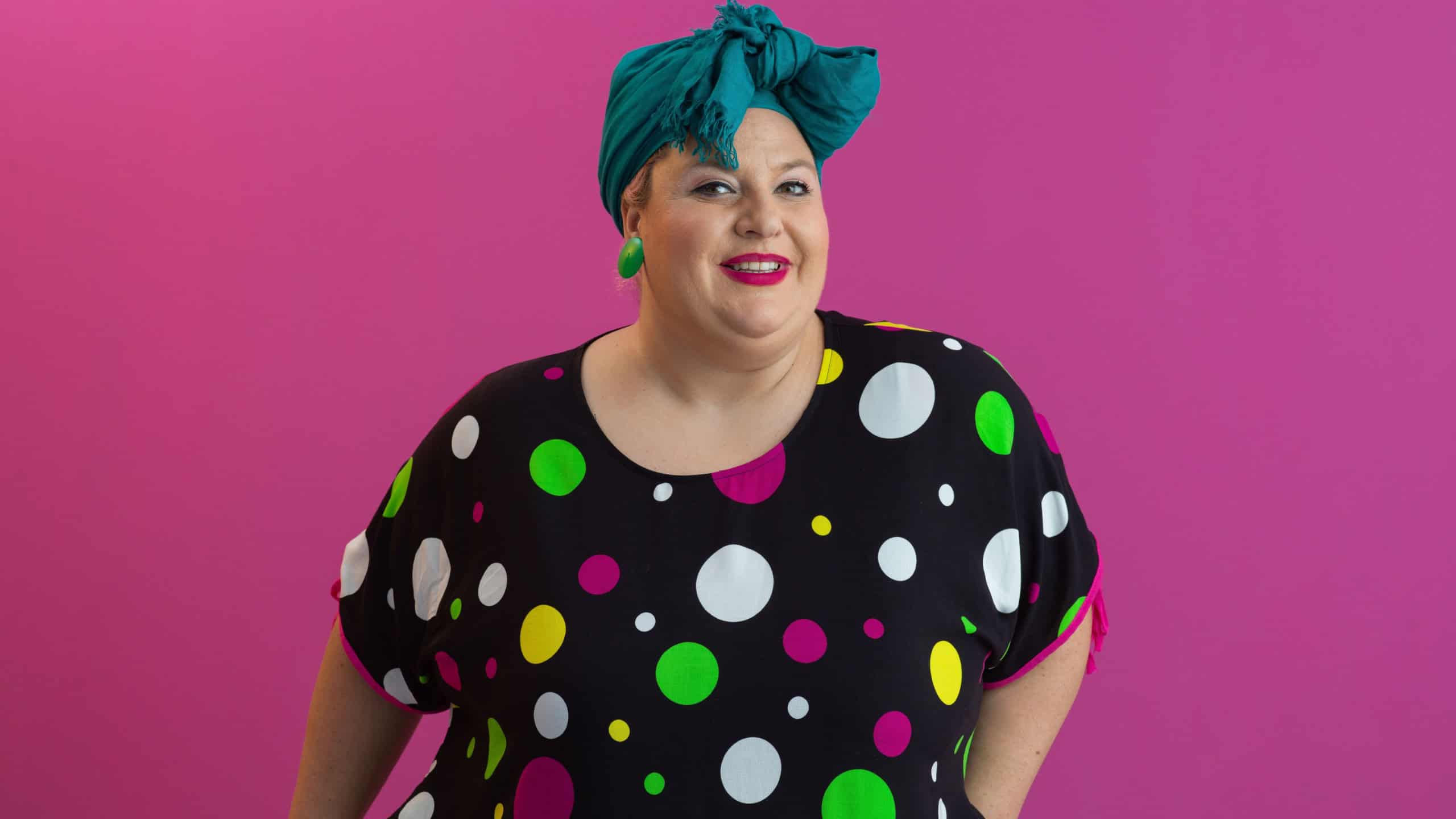 Happy plus size woman smiling in colorful outfit against pink background