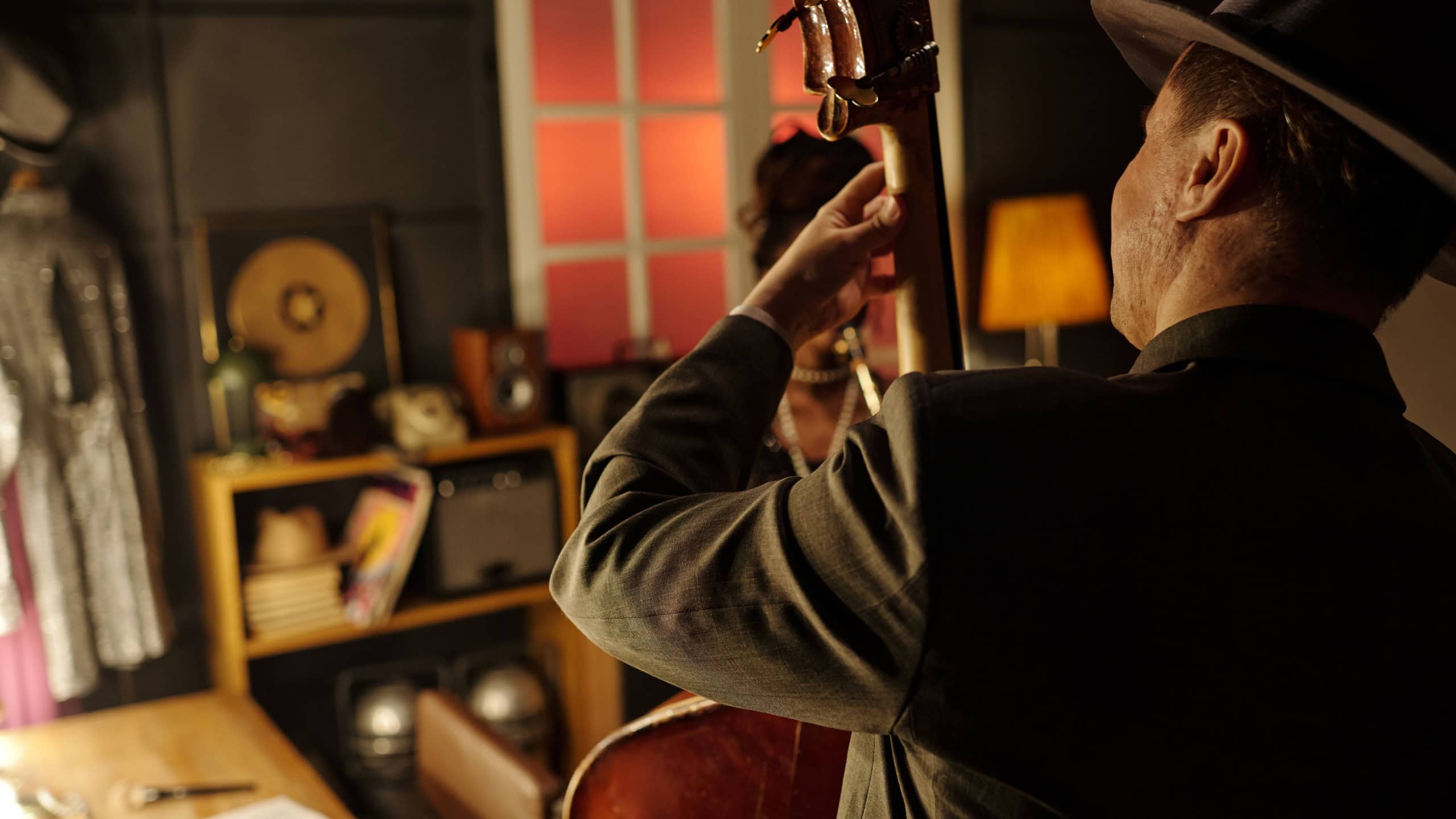 Middle aged Caucasian man playing upright bass in jazz band, standing in warmly lit studio with musical instruments and vintage decor, focusing on performance with hands on instrument