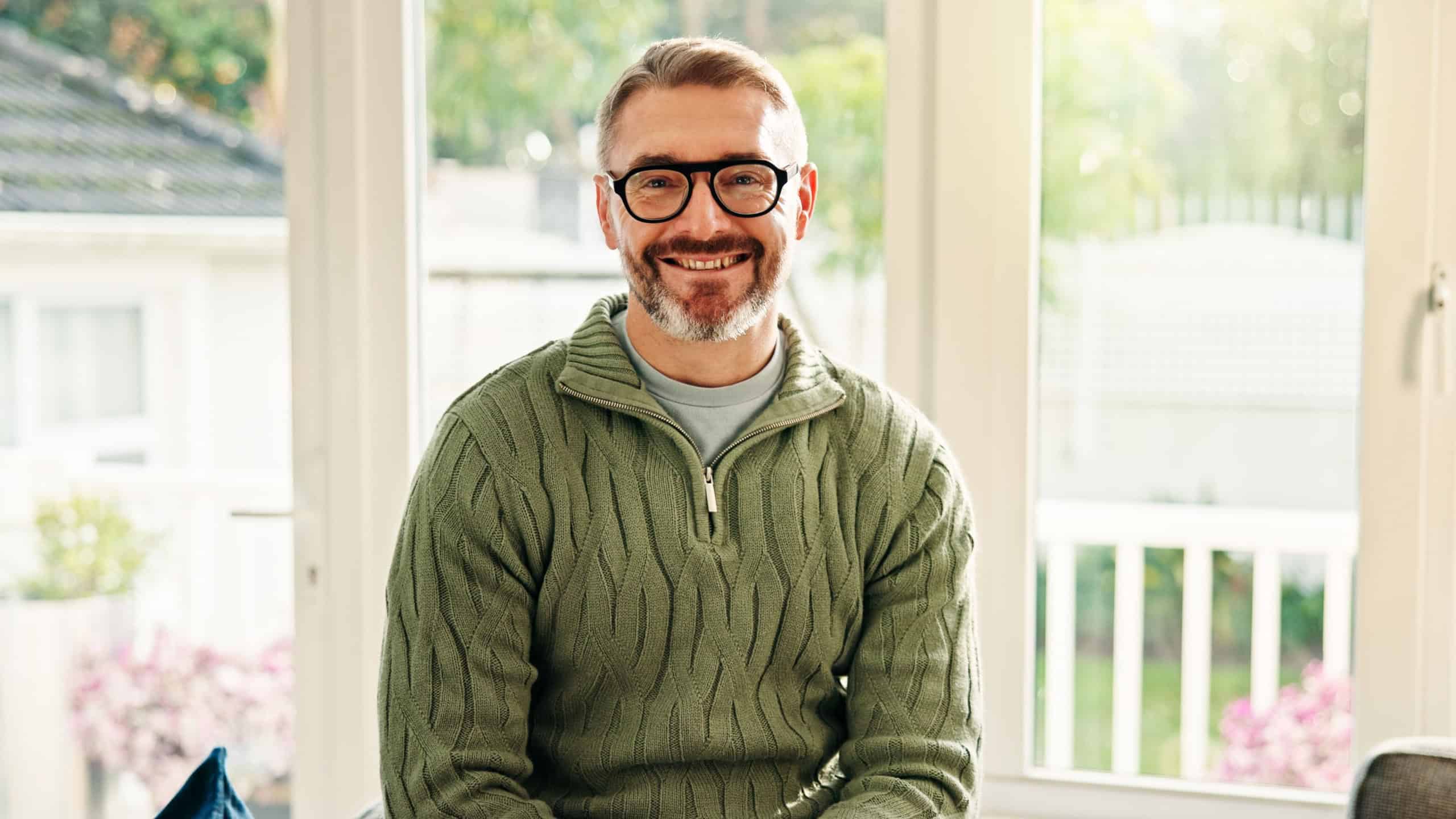 Portrait, mature and happy man in home for relax, peace and calm on weekend break in apartment. Glasses, smile and person chill in living room for staycation, wellness and confidence in Australia