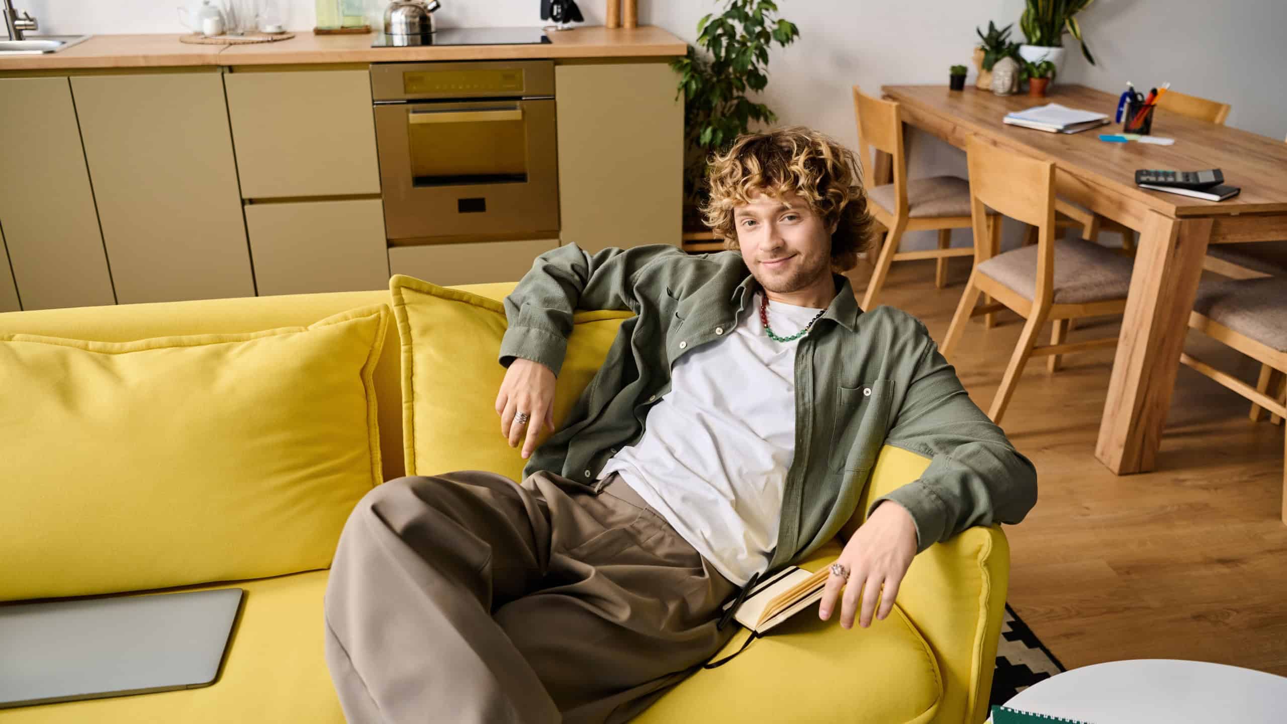 A handsome man sits casually on a bright yellow sofa, enjoying a moment of relaxation at home.