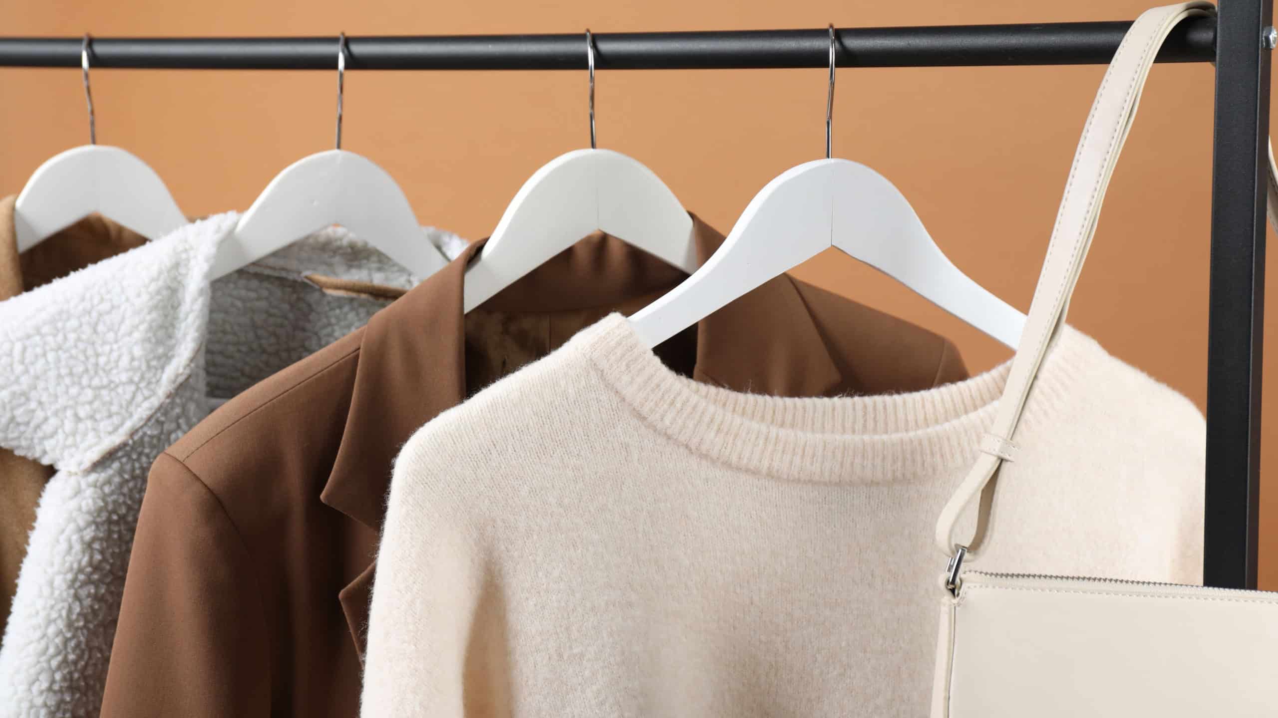 Different clothes and bag hanging on rack against brown background, closeup