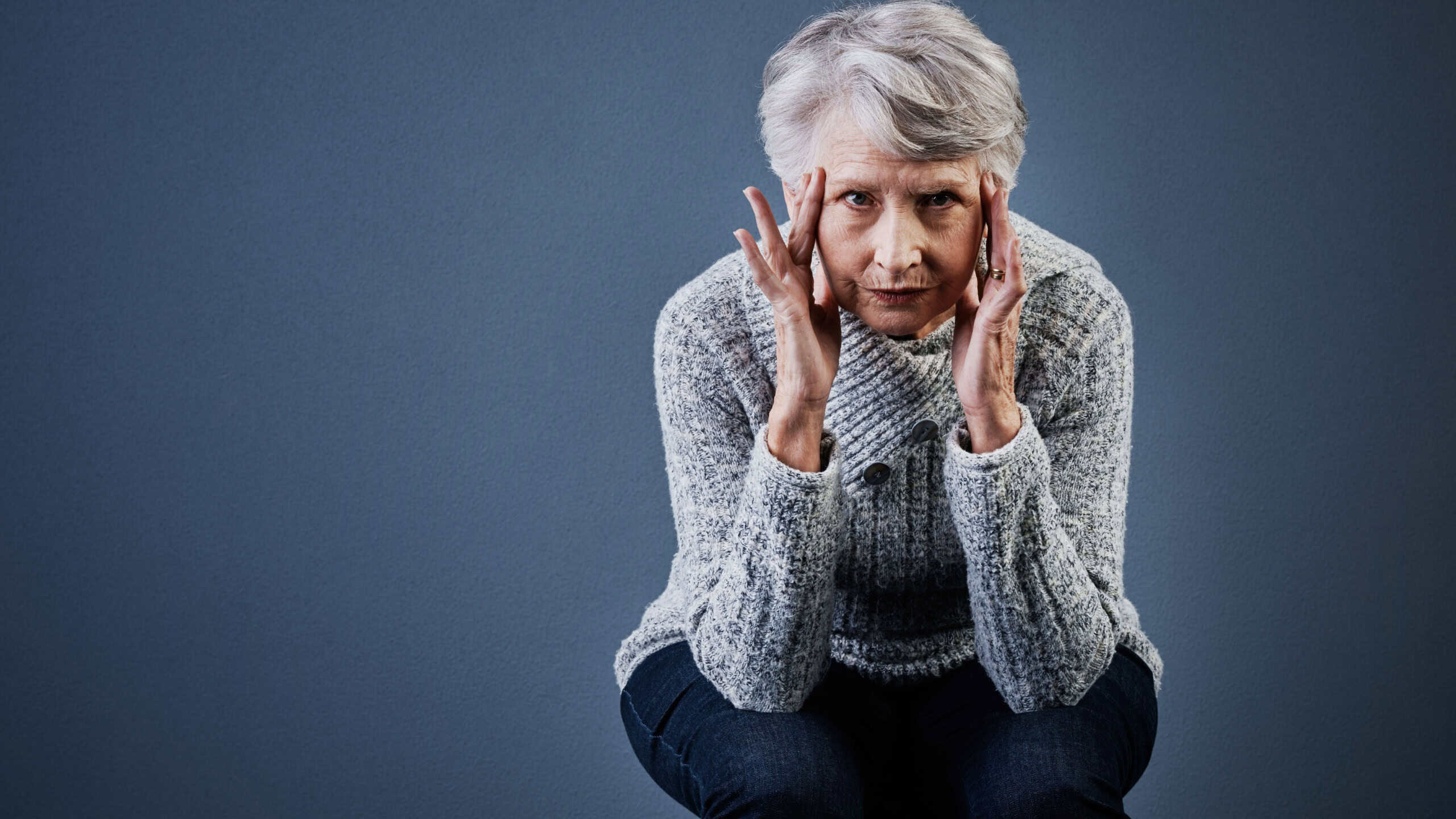 Mental health, portrait and stress with old woman on gray background for psychology or wellness. Headache, retirement and space with senior person in studio for alzheimer or dementia awareness