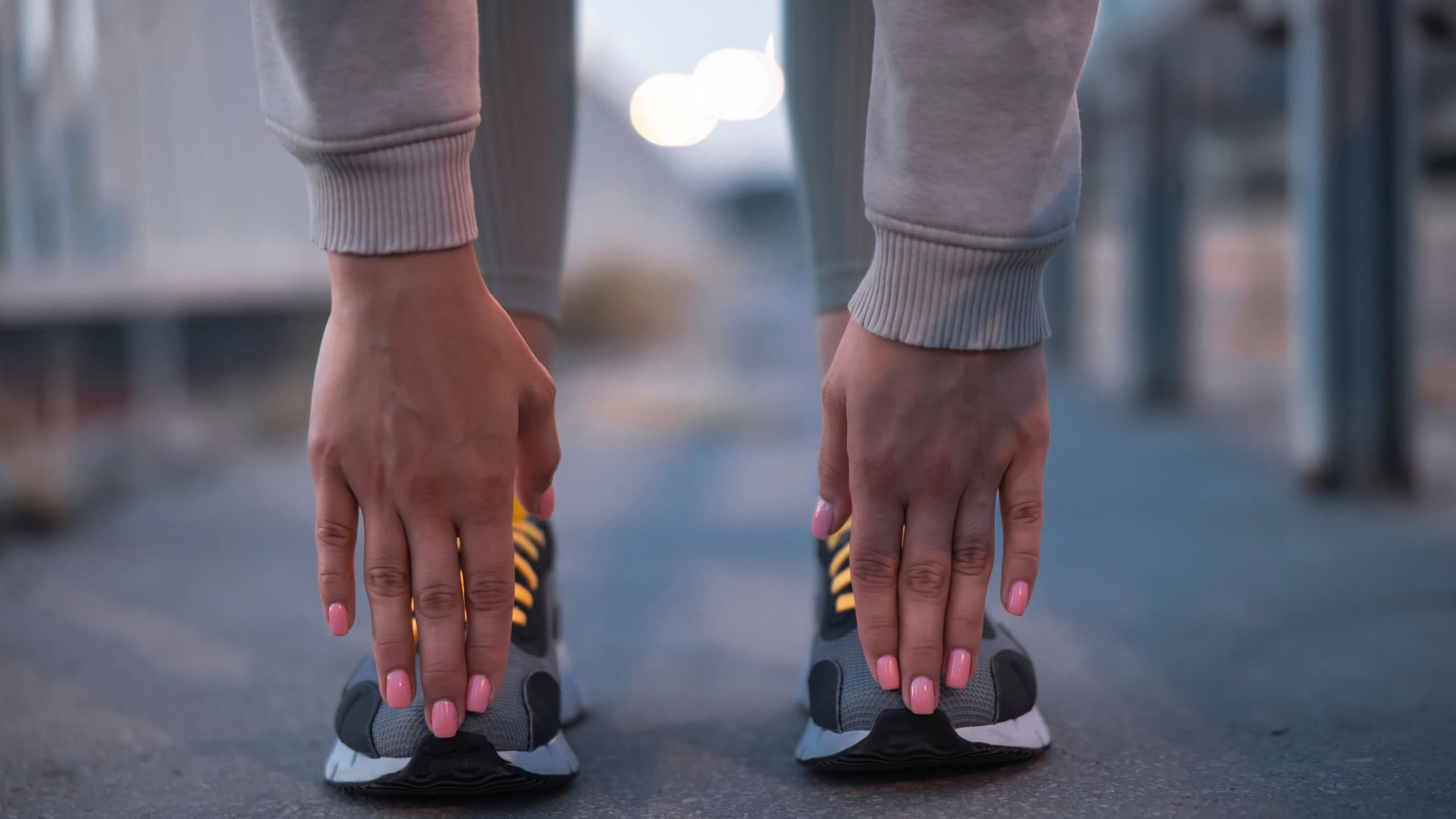 Detail of an active fit woman in sportswear stretching out and warming up for morning jogging at dawn, fingers touching toes