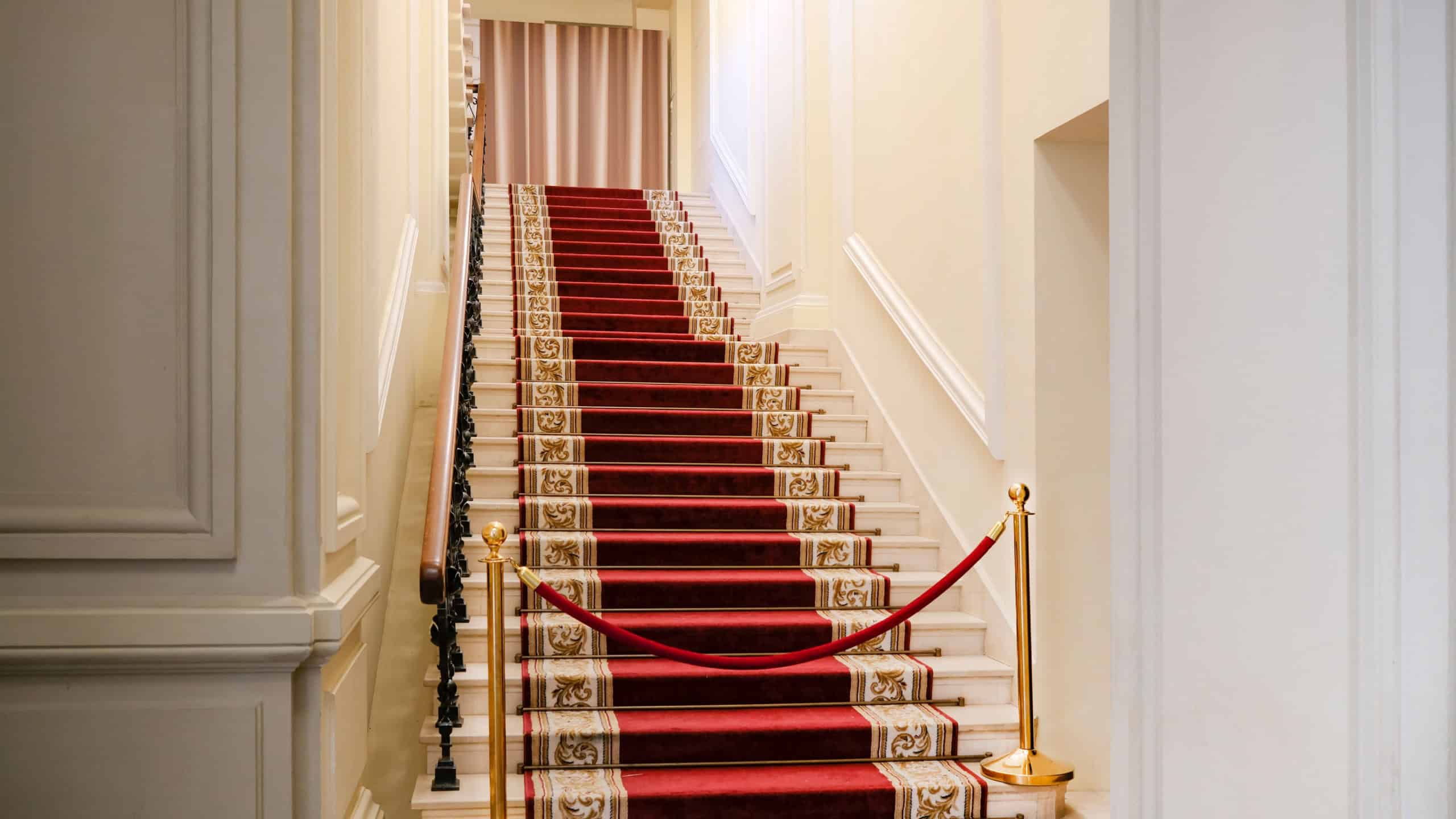 A red carpet and a staircase leading up to the hall. The grand staircase with its red carpet and golden pillars creates a sense of importance and prestige.