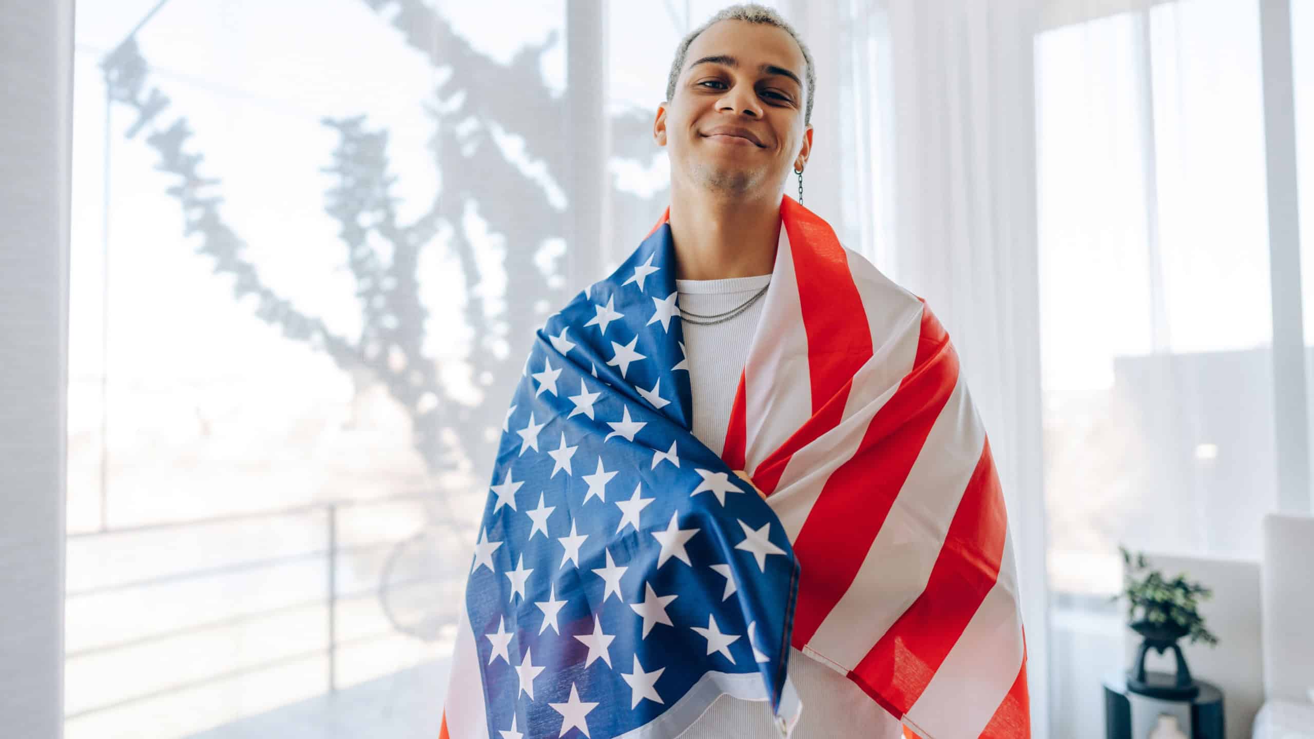 Proud young man holding the American flag on a sunny day. Concept of patriotism, 4th of July celebration, and national pride