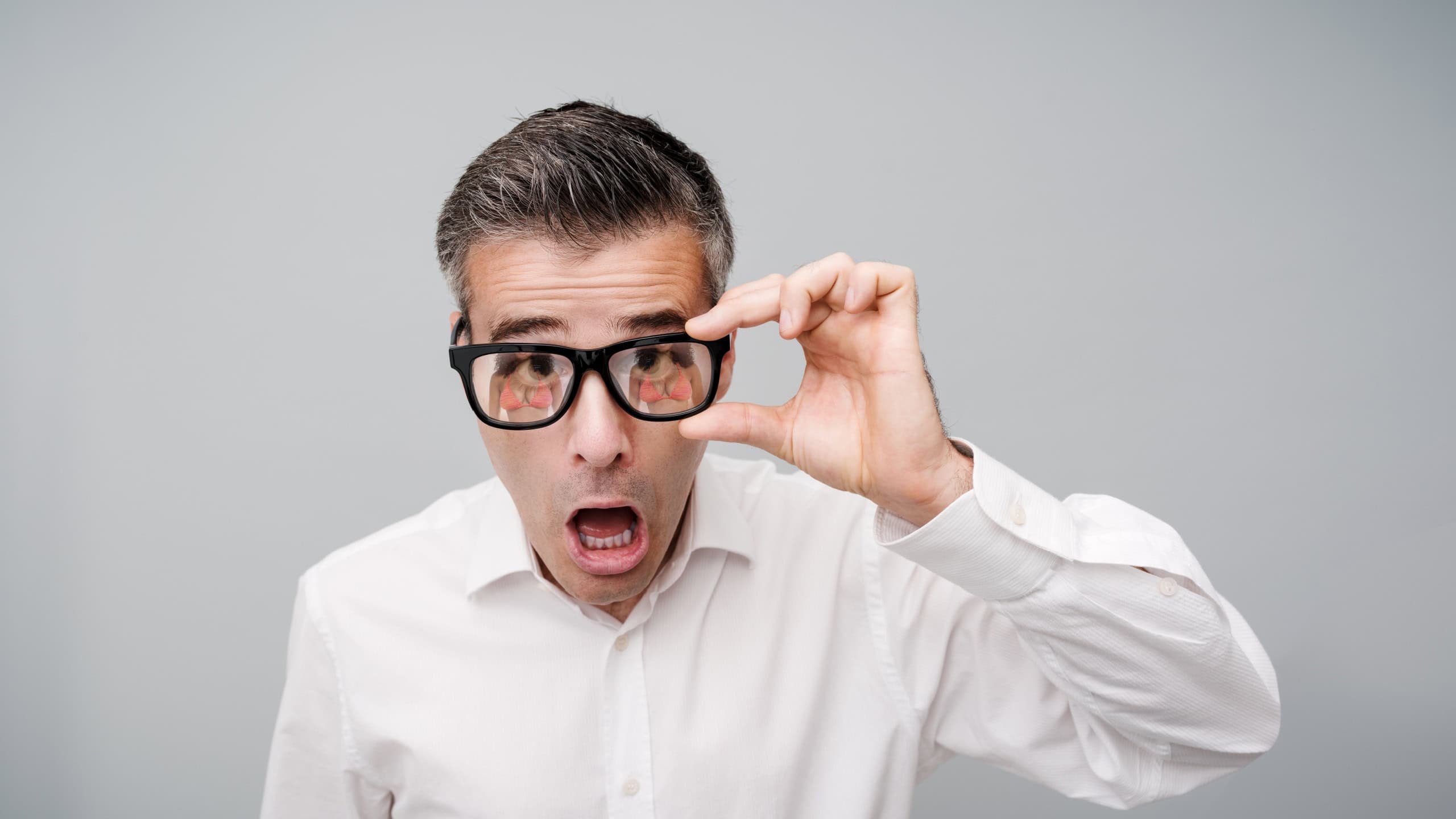 A distraught man stares at the camera and adjusts his glasses. He can't believe his eyes: a woman in a bikini is reflected in the lenses of his glasses.