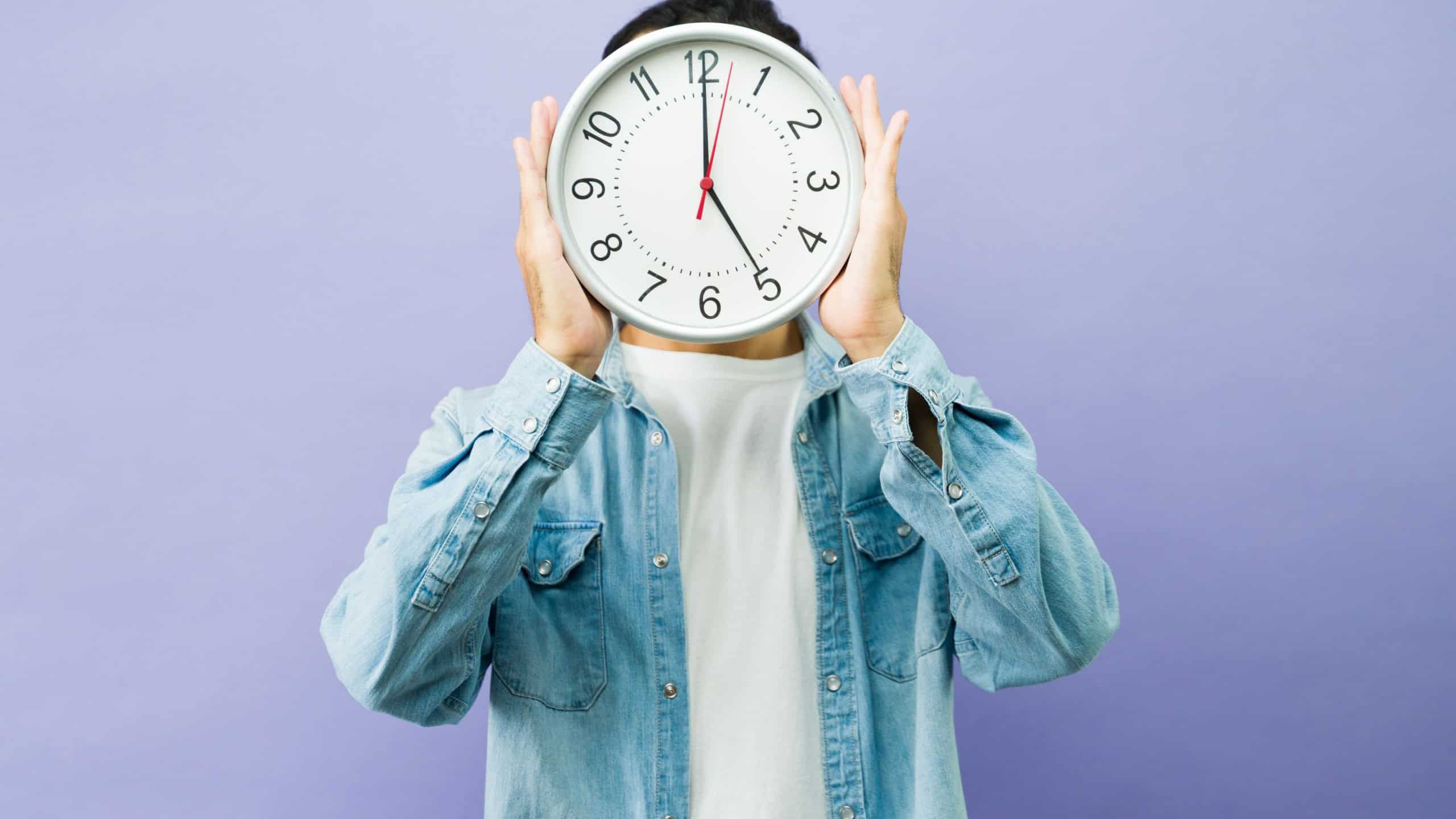 Man covering face with a clock, representing concepts of time, schedule, punctuality, and managing workload in a studio