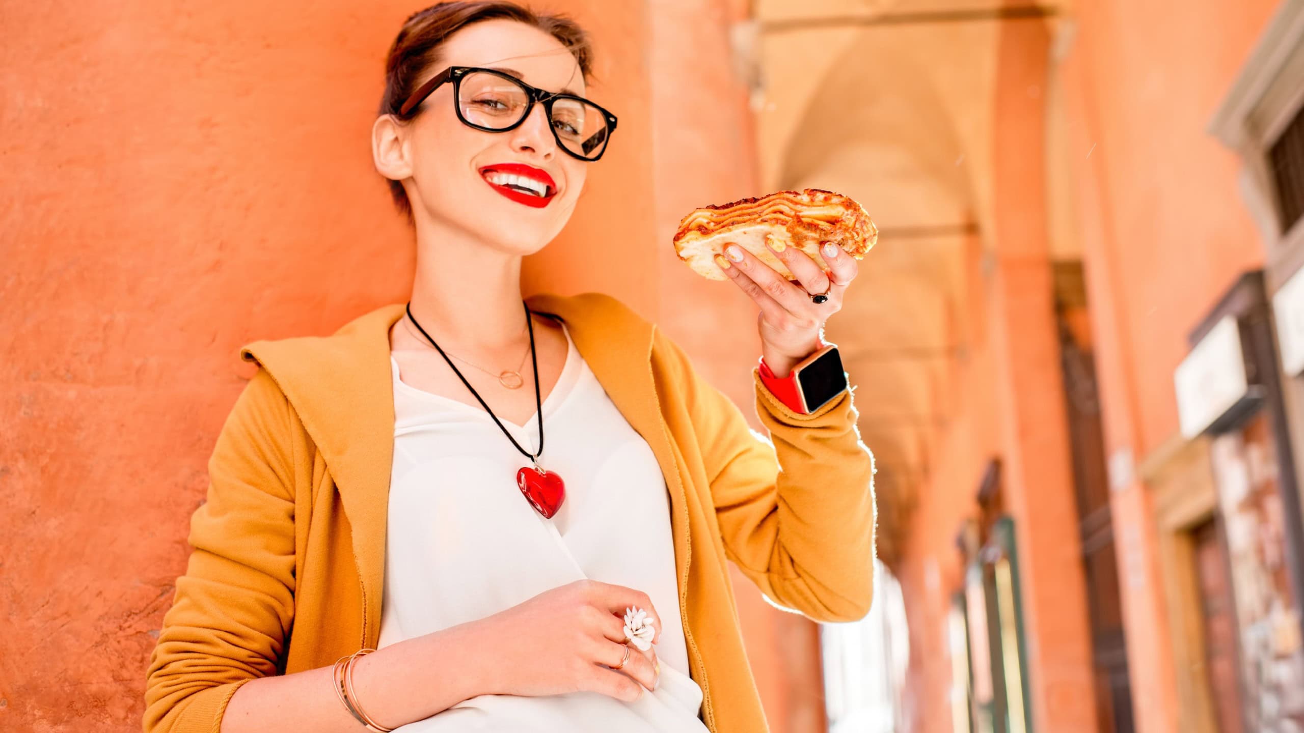 Young woman eating lasagna with bolognese outdoors on the street in Bologna city in Italy. Lasagna bolognese was invented in Bologna city. Soft focus with small depth of field