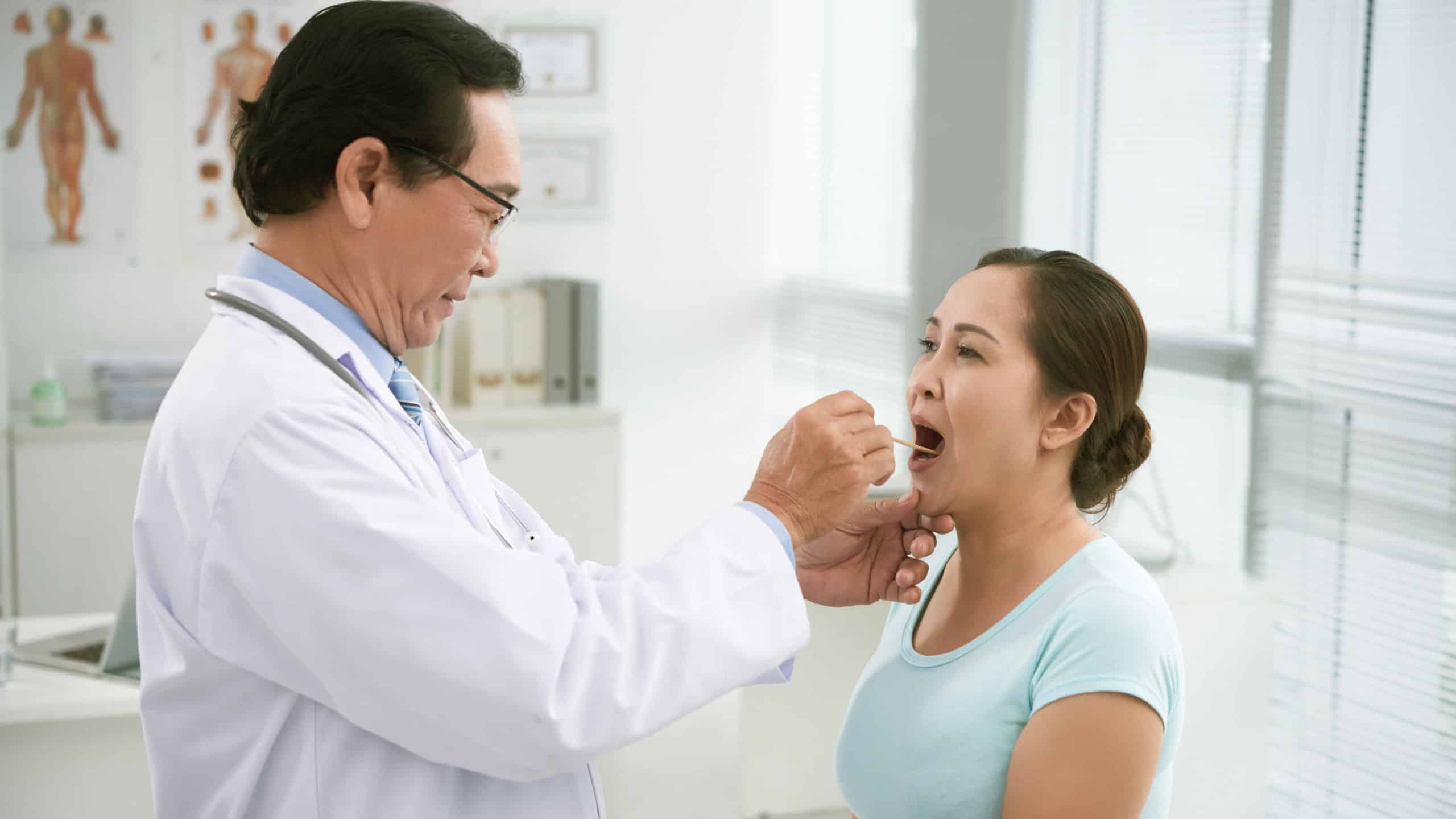 Doctor using tongue depressor to examine throat of patient