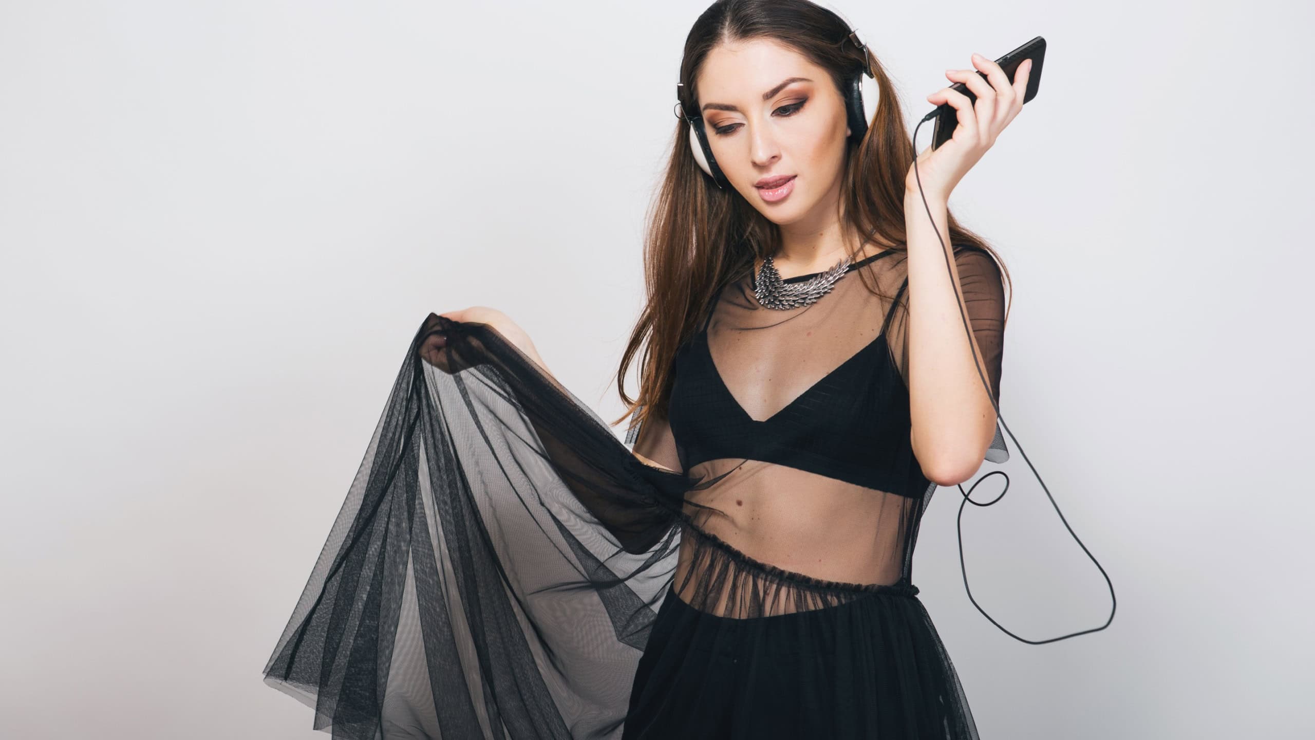 young beautiful woman in stylish outfit, black transparent tunic, top, bohemian style, fashion trend, listening to music headphones, party, having fun, happy smiling, positive, enjoying sound, dancing