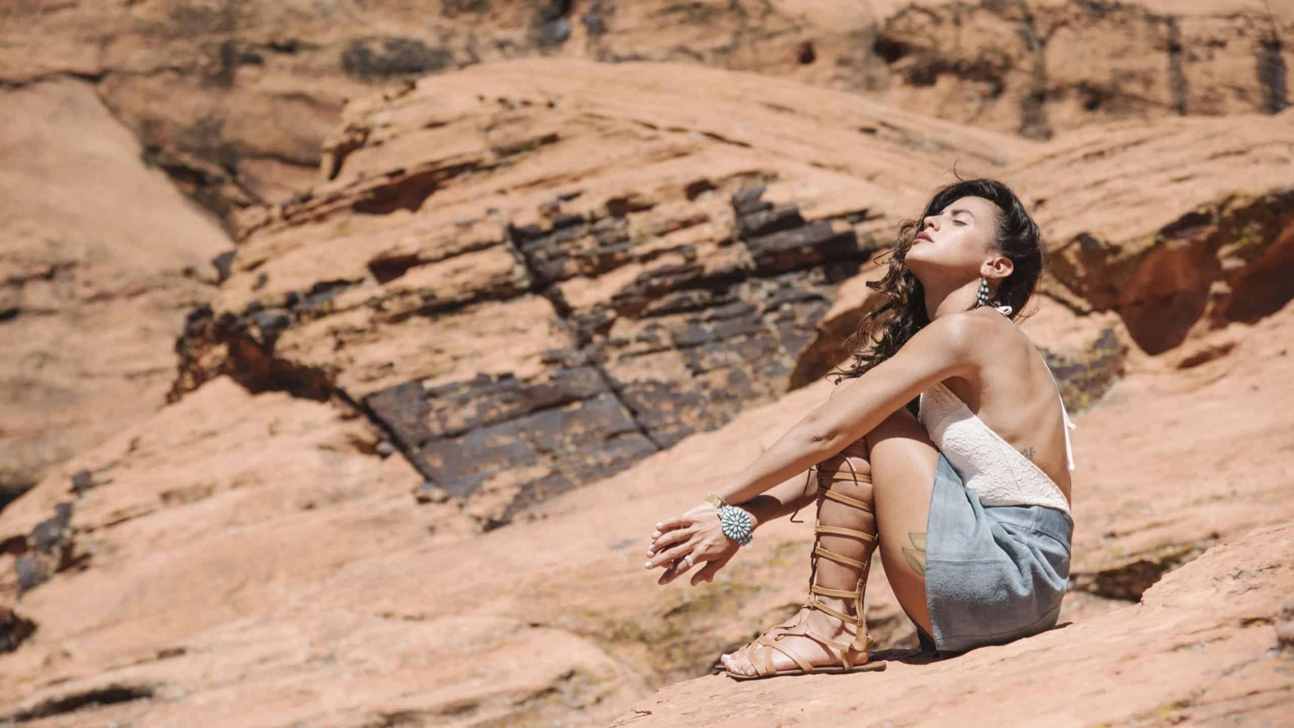 Young woman with long brown hair sitting on a rock in a canyon,