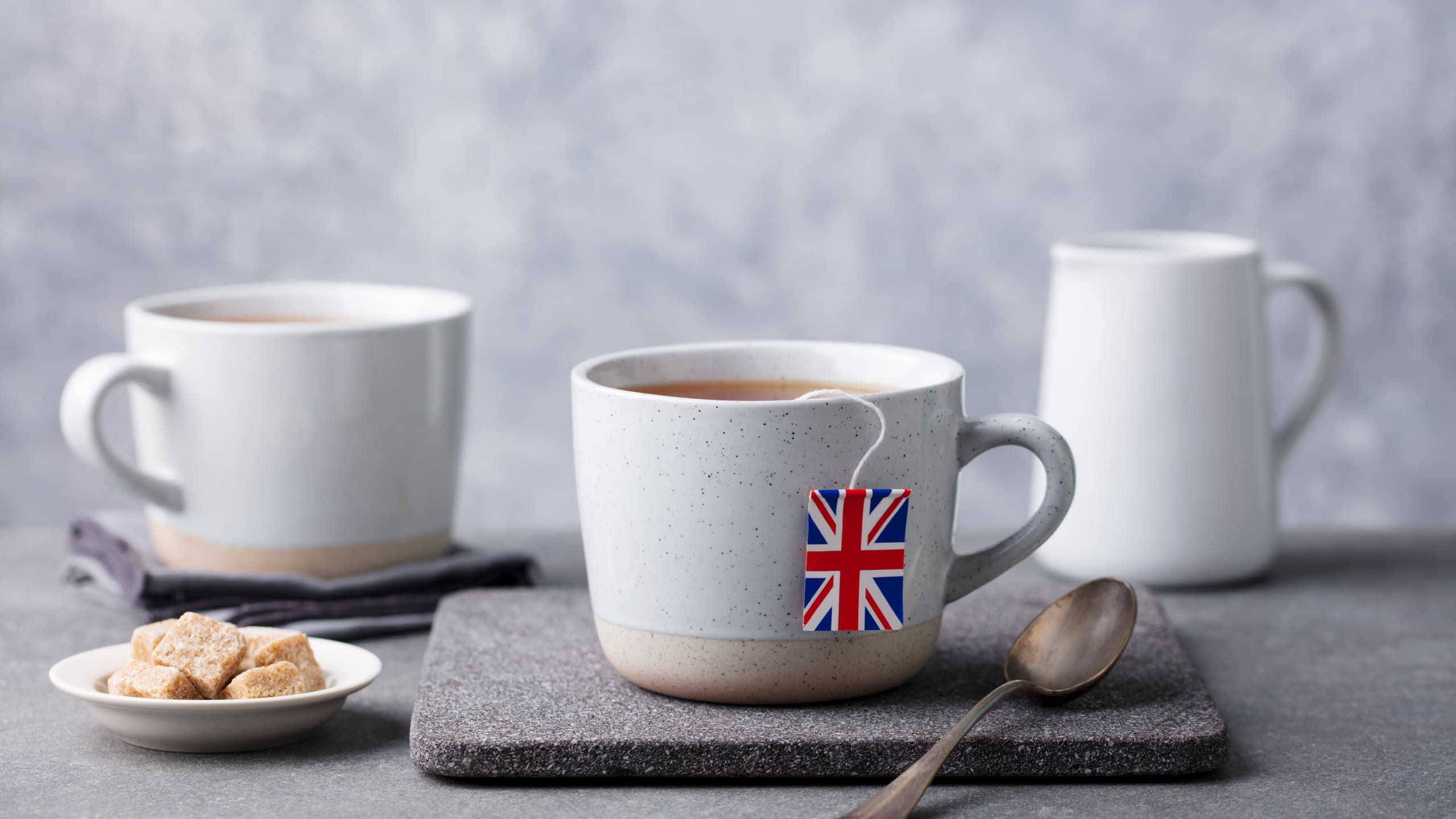 Tea in mugs with British flag tea bag label. Grey background. Copy space.