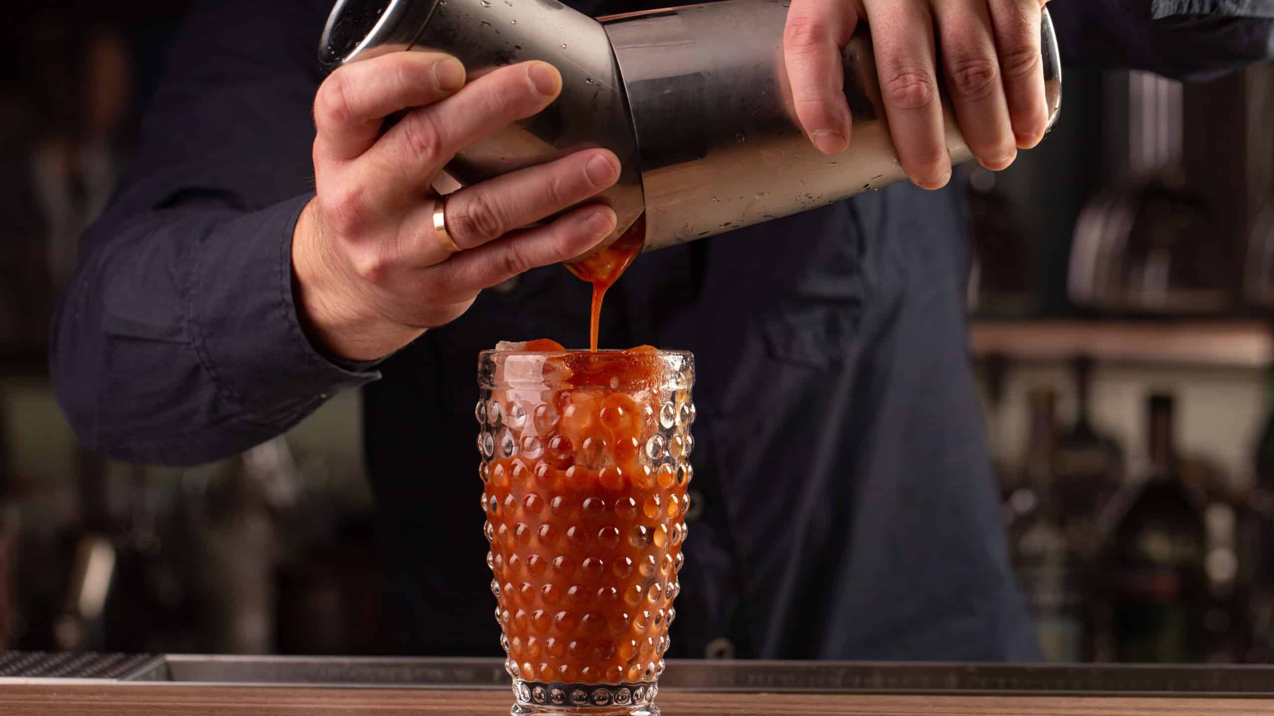 bartender pours tomato red juice from the shaker, making a cocktail, drink