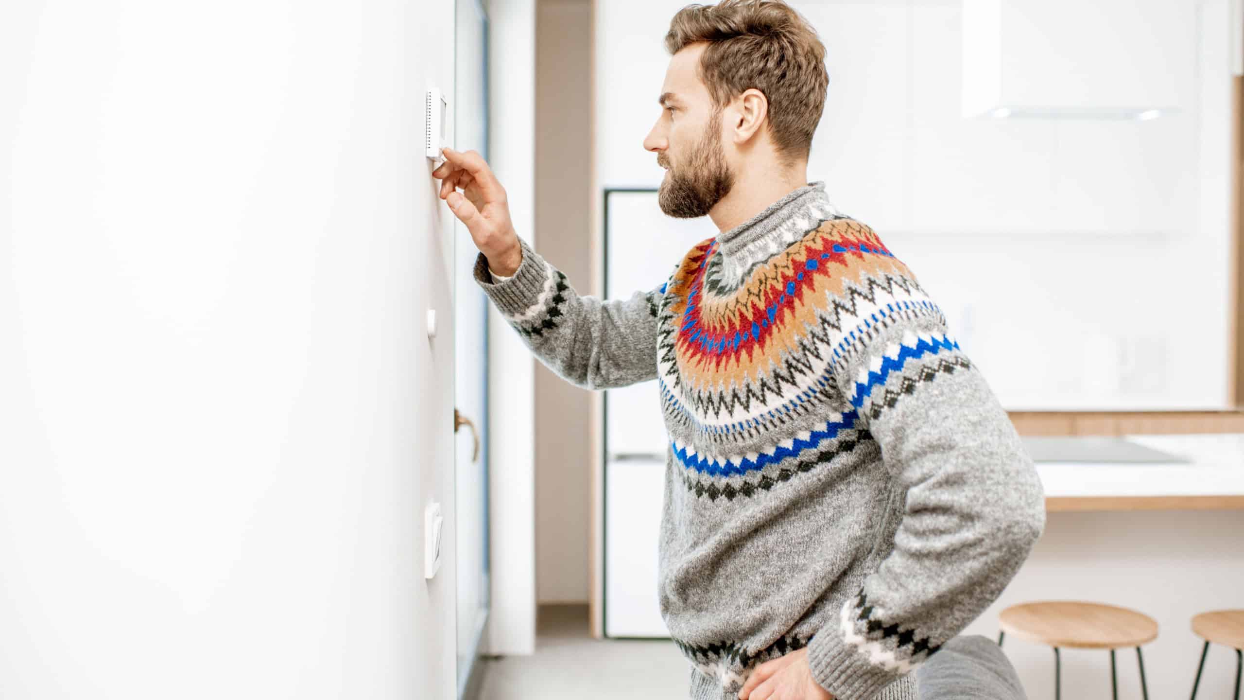 Man in sweater adjusting room temperature with electronic thermostat at home