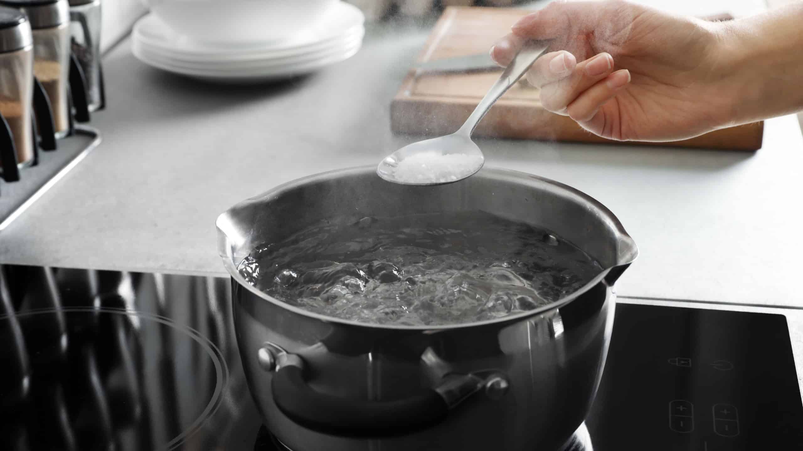 Woman salting boiling water in pot on stove, closeup