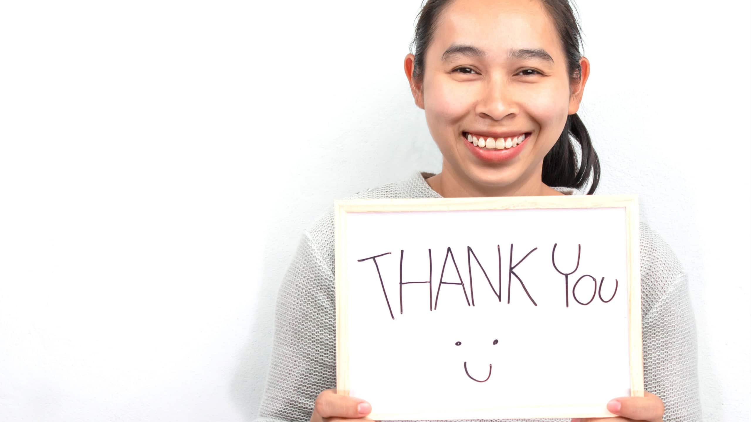 Studio shot of Asian woman holding a Thank you sign writing on whiteboard with handwriting. Isolated on white background.