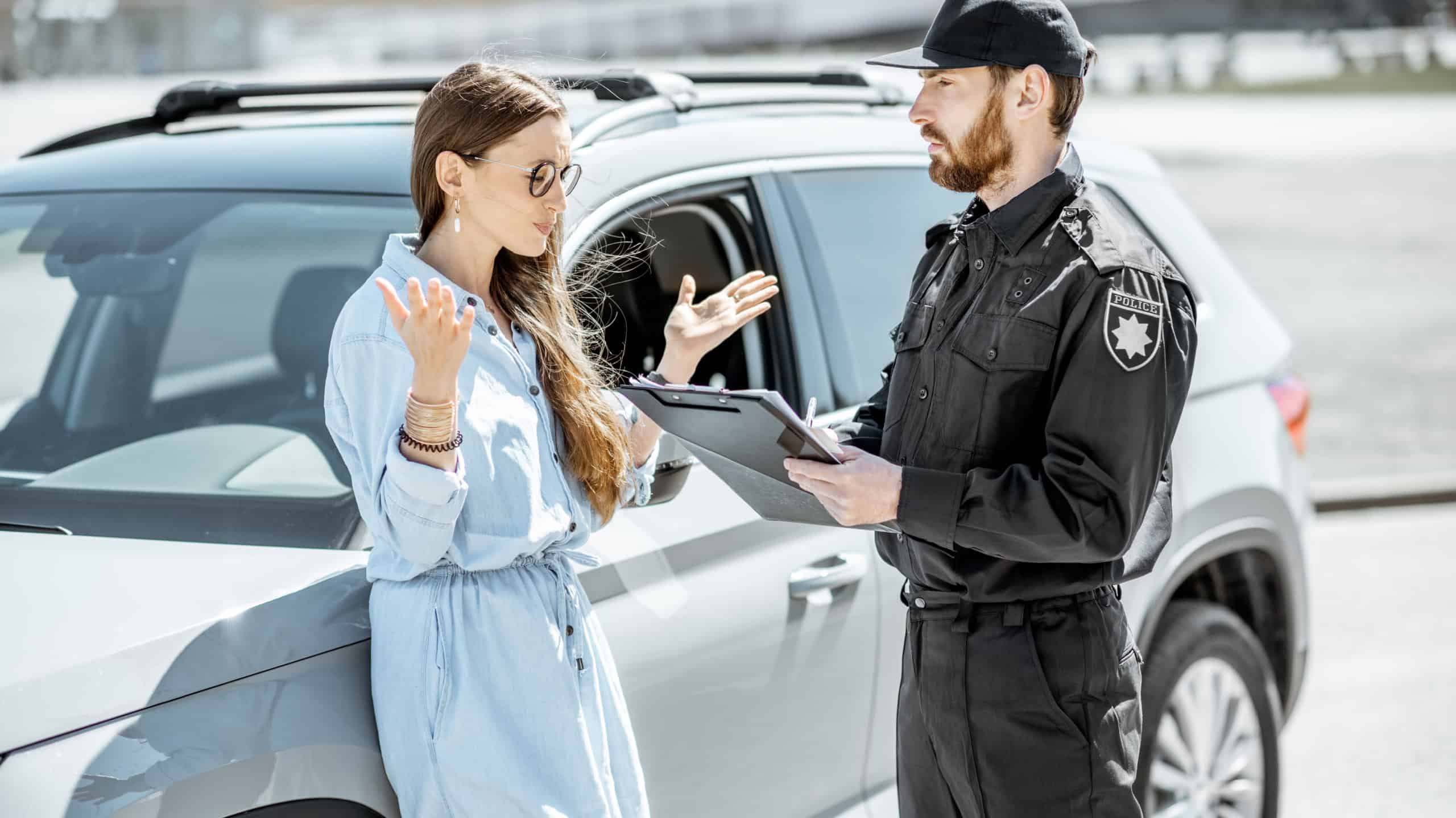 Policeman arguing with female driver while issuing fine for violating the traffic rules on the roadside near the car