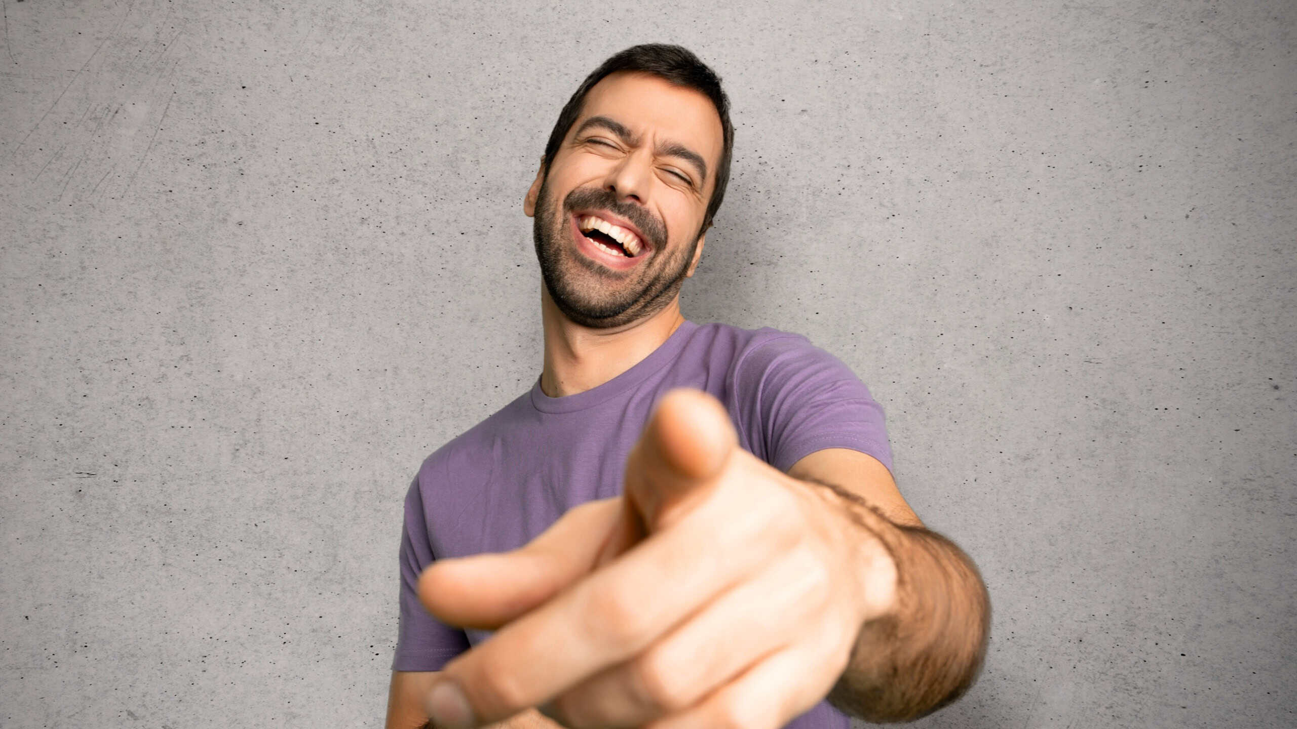 Handsome man pointing with finger at someone and laughing a lot over textured wall