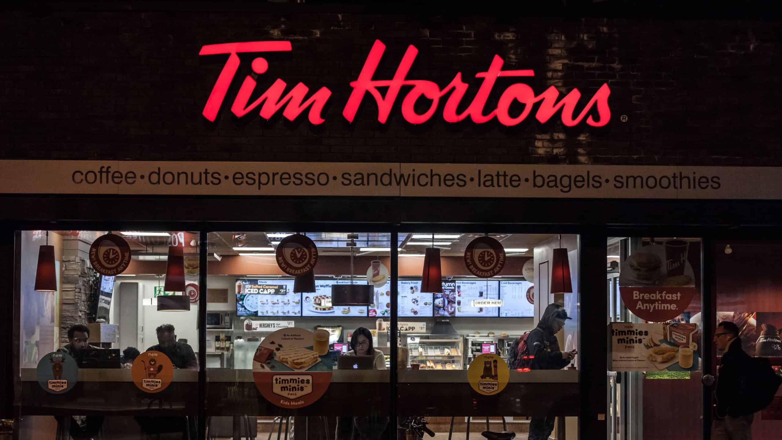 TORONTO, CANADA - NOVEMBER 14, 2018: Tim Hortons logo in front of one of their restaurants in Toronto, Ontario, at night, with pedestrians passing. Tim Hortons is a cafe and fastfood canadian brand