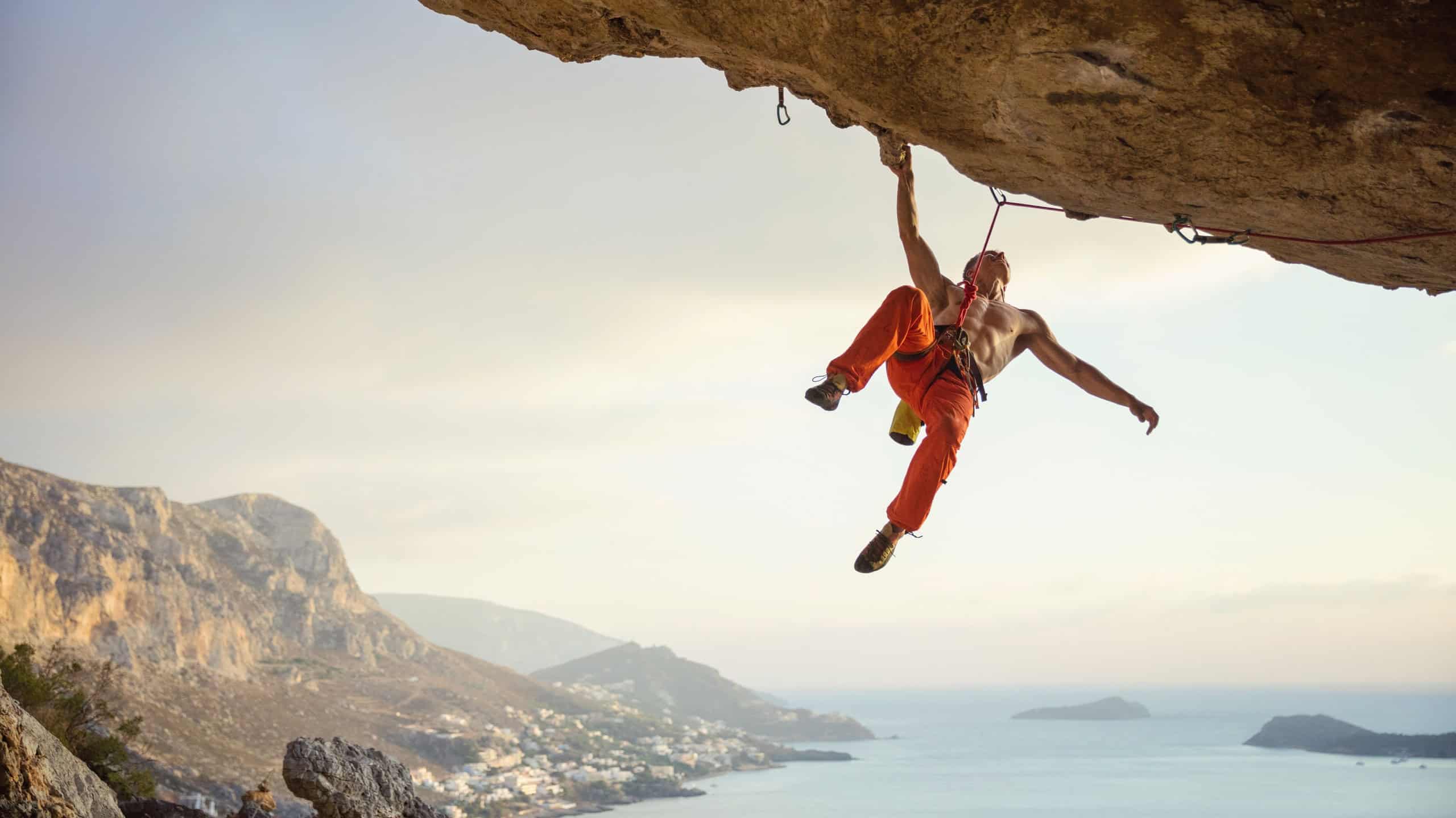 Young man climbing challenging route in cave against beautiful view of coast
