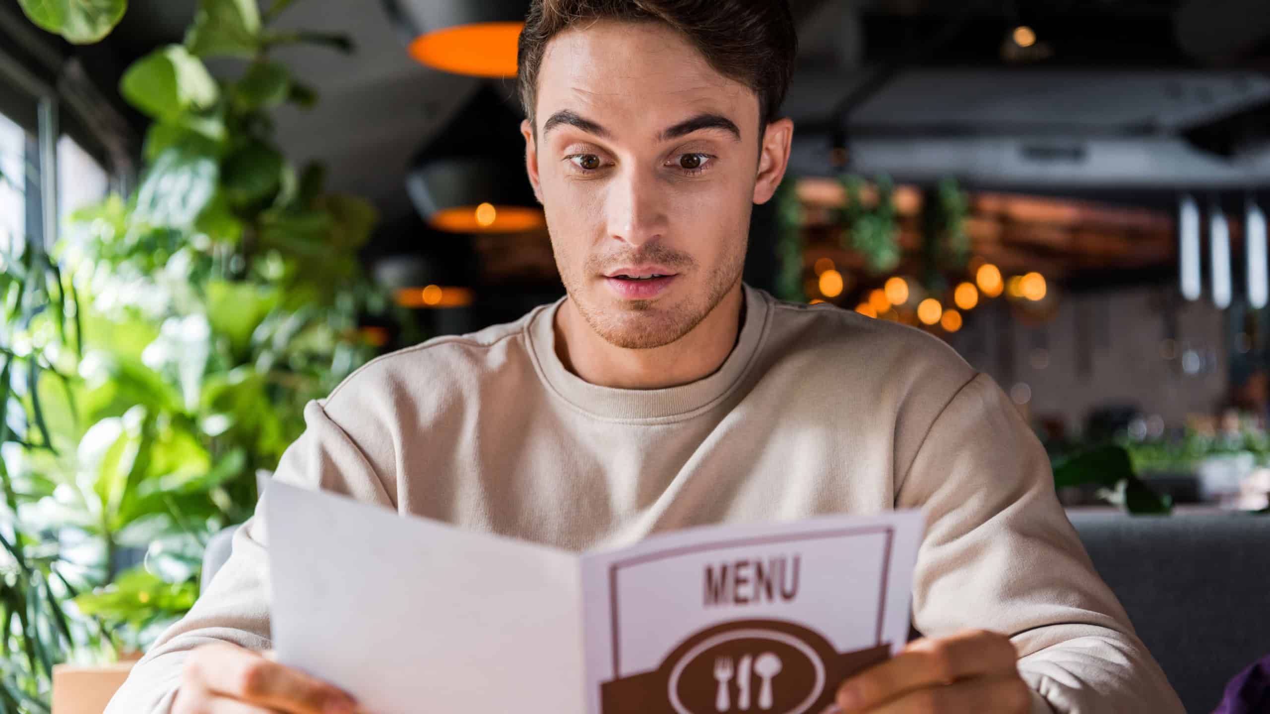 selective focus of surprised man holding menu in restaurant