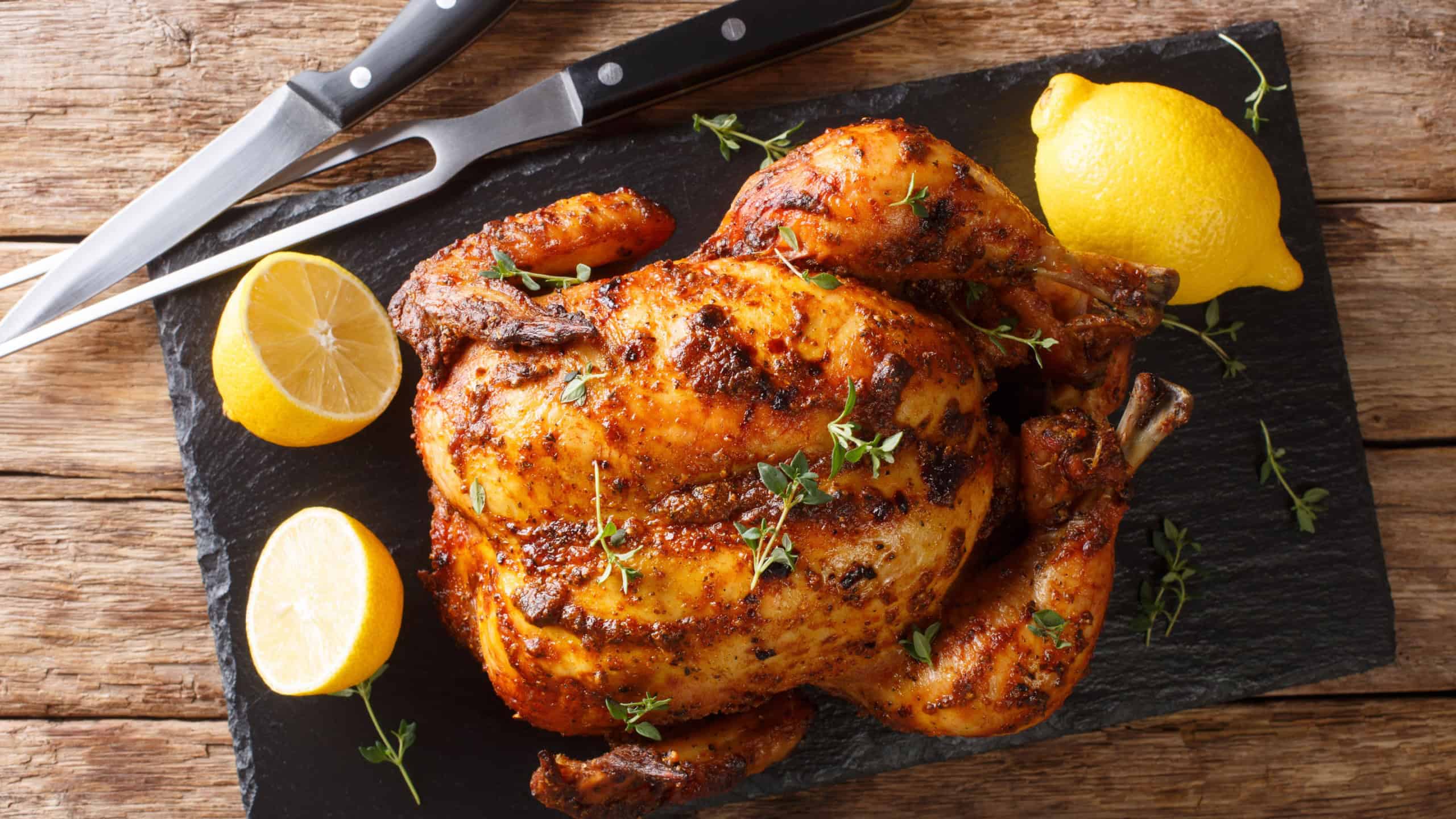 Homemade chicken rotisserie with thyme, lemon closeup on a slate board on the table. Horizontal top view from above