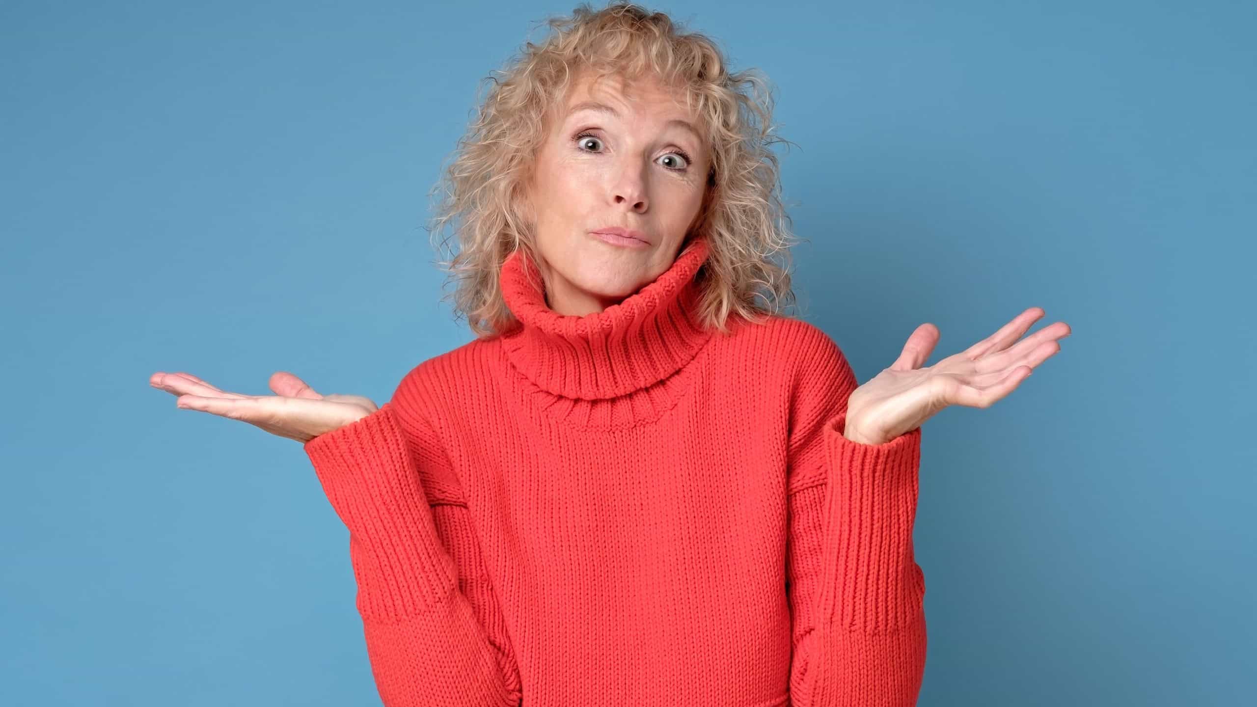 Quizzically attractive senior female in red sweater on blue background. Mother does not know right solution. studio shot
