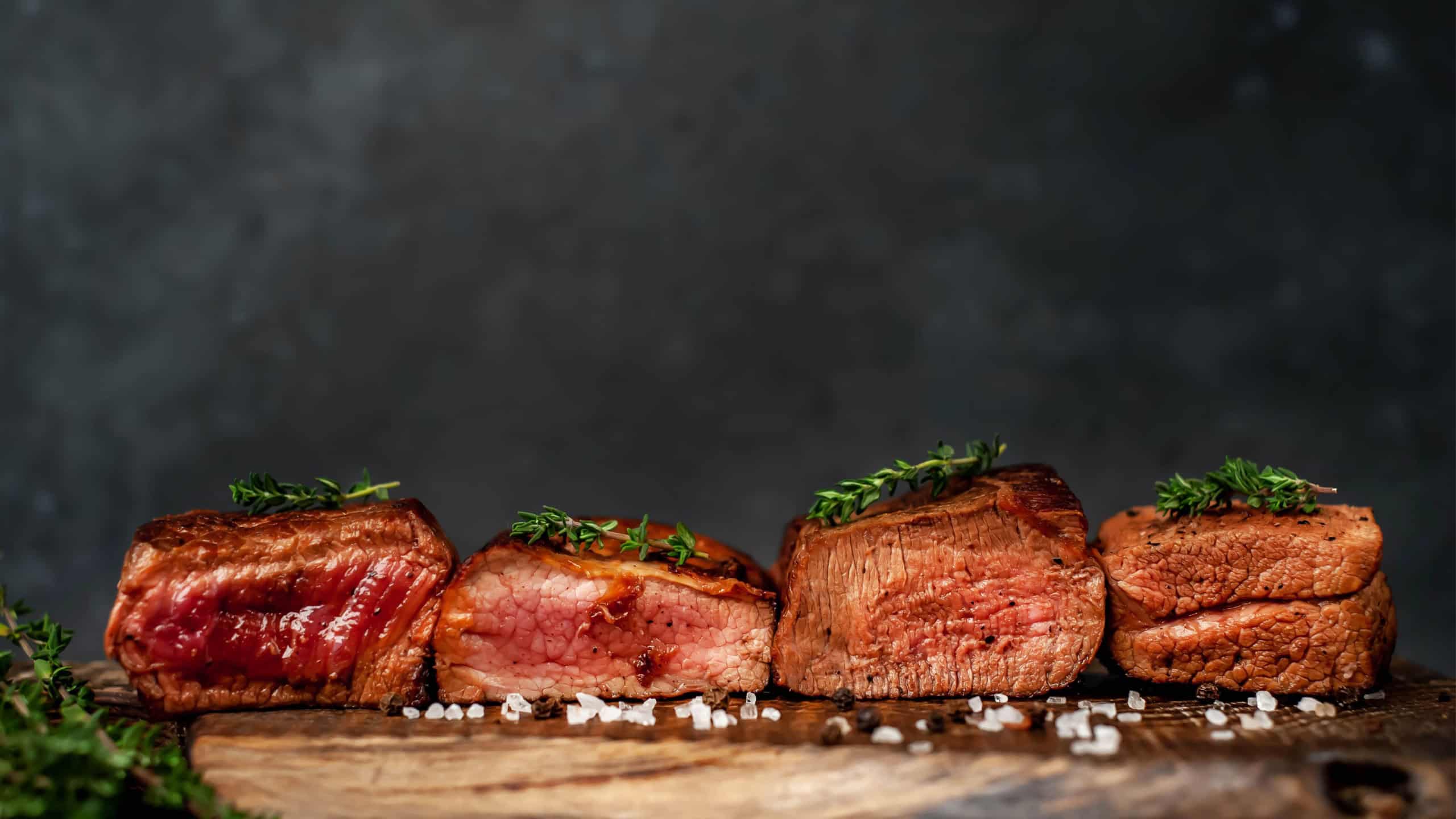 four grilled steaks with spices on a stone background. Four types of meat frying Rare, Medium, Medium Well, Well Done