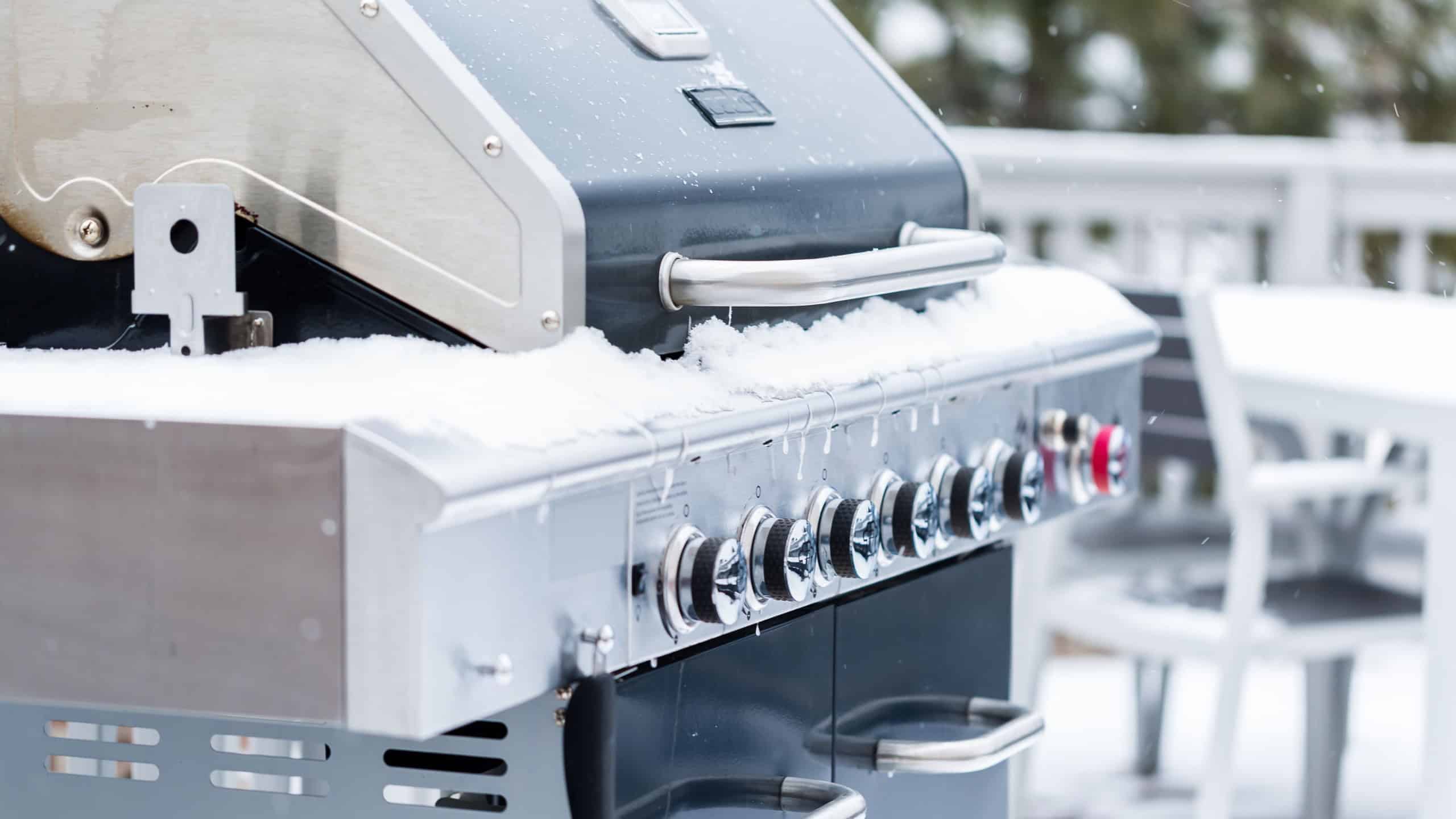 Outdoor grill covered with snow on residential back patio in the Winter.