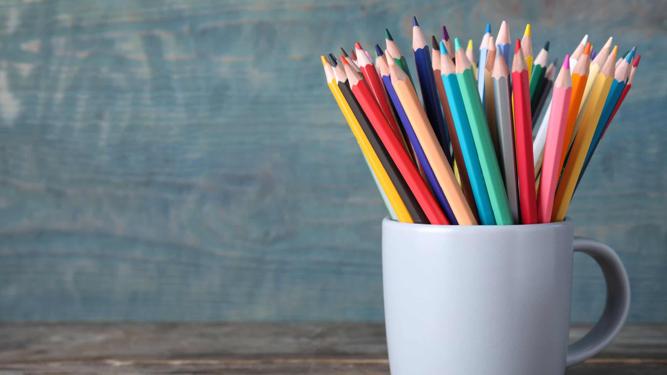 Colorful pencils in cup on wooden table. Space for text