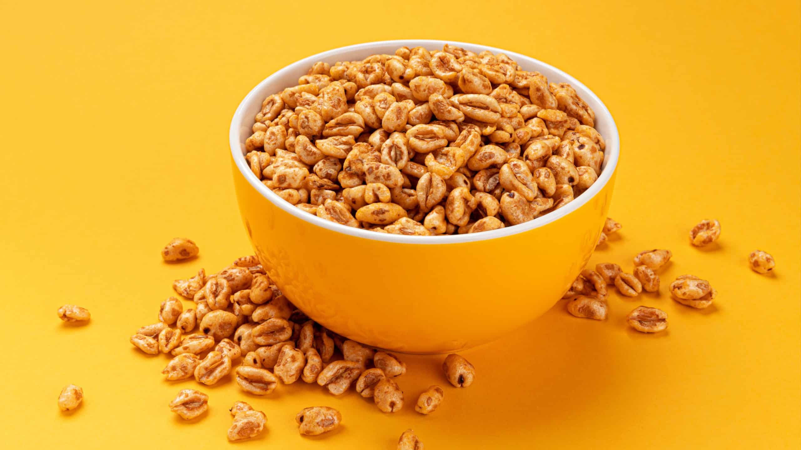 Puffed wheat cereal in bowl on yellow background, honey air rice
