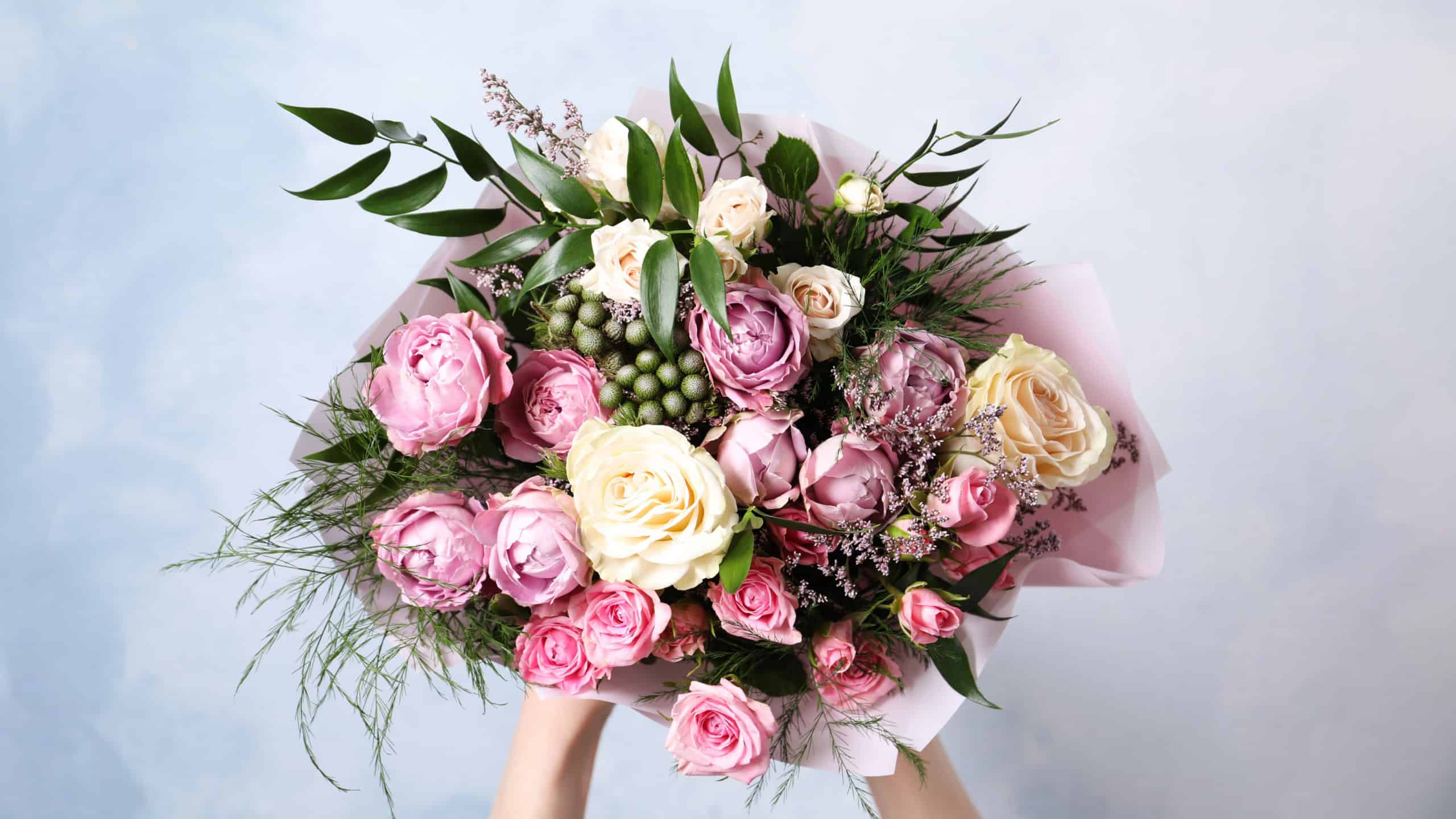 Woman with bouquet of beautiful roses on light blue background, closeup