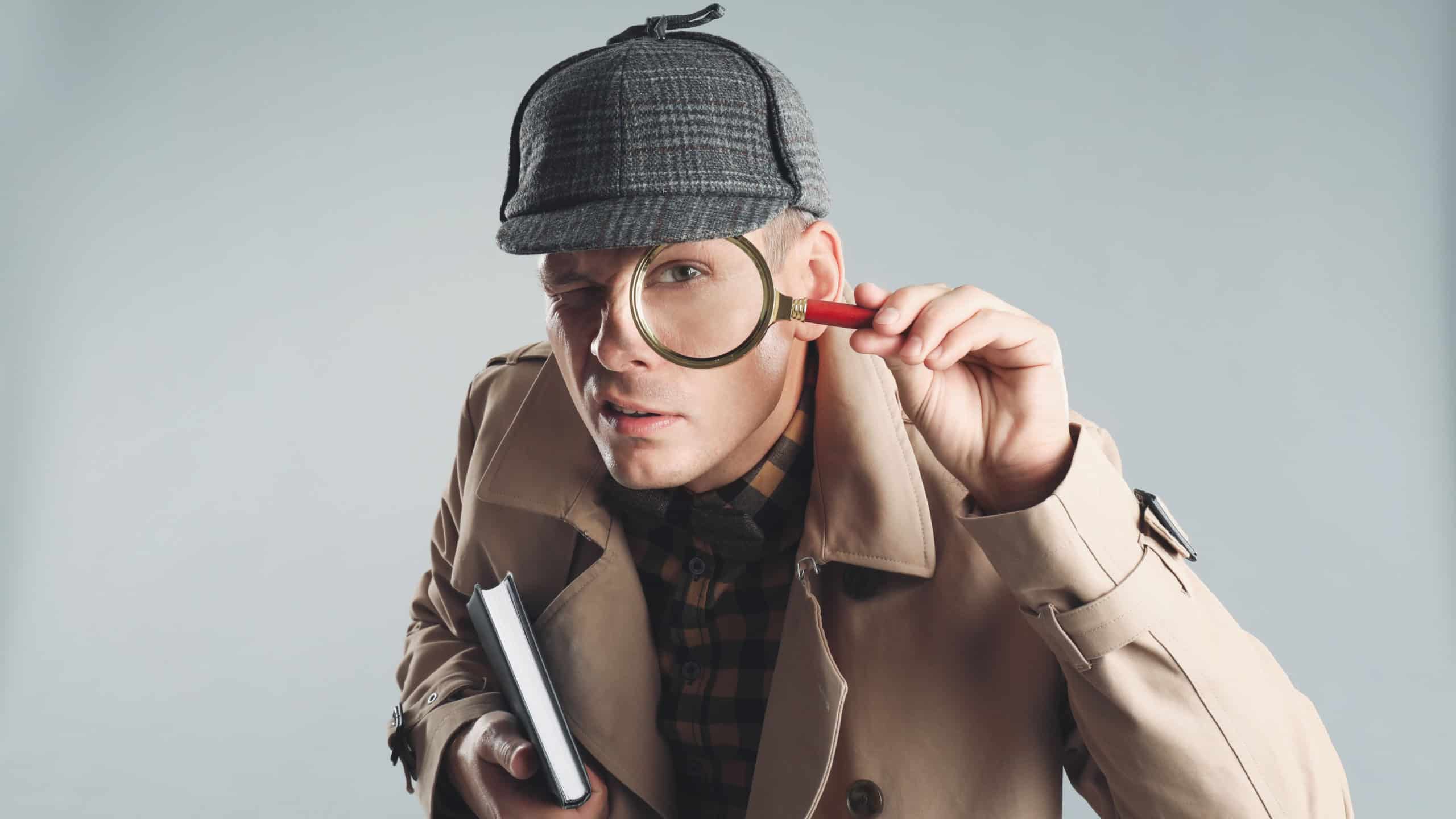 Male detective looking through magnifying glass on grey background