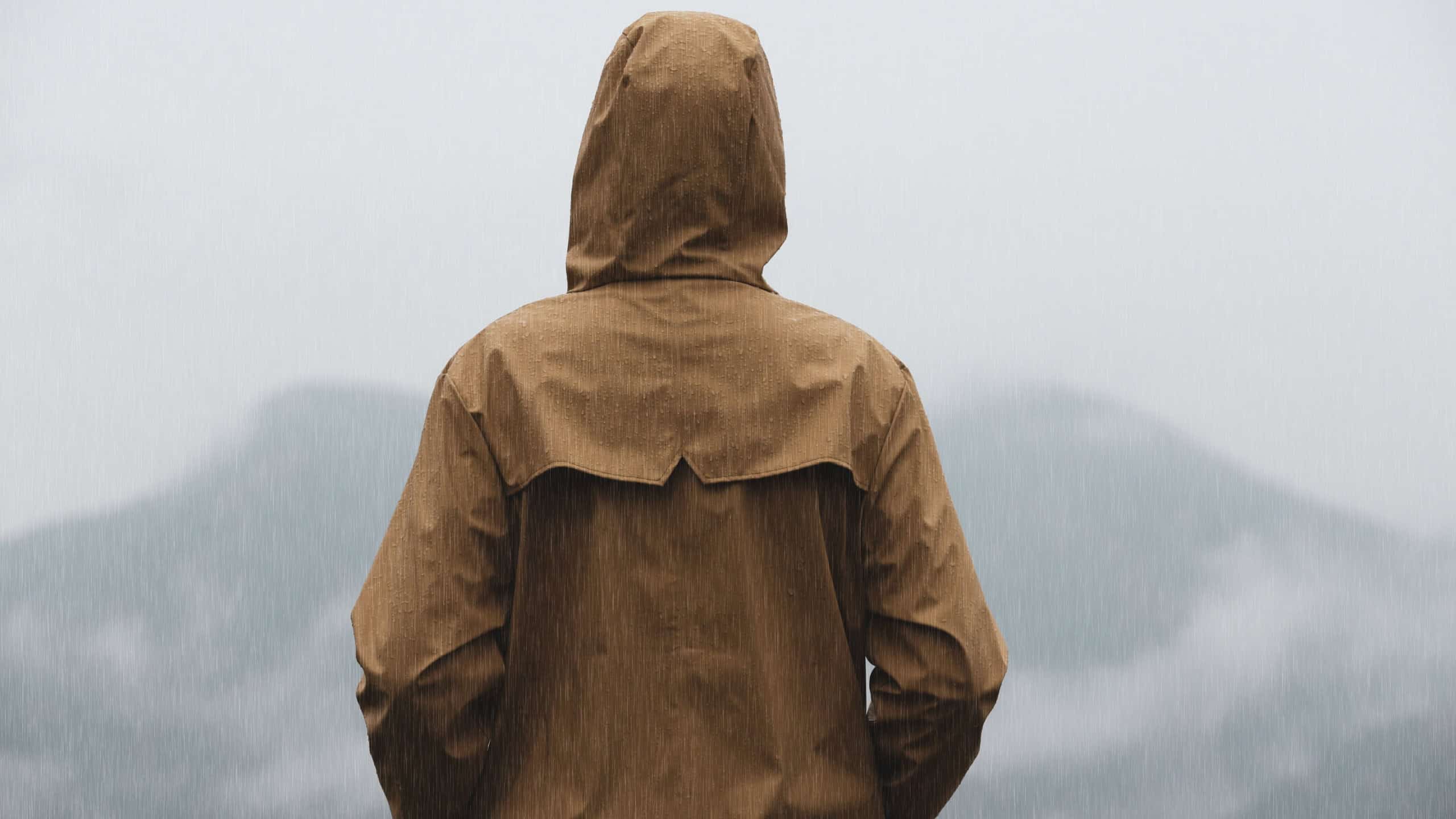 Woman in raincoat enjoying mountain landscape under rain, back view
