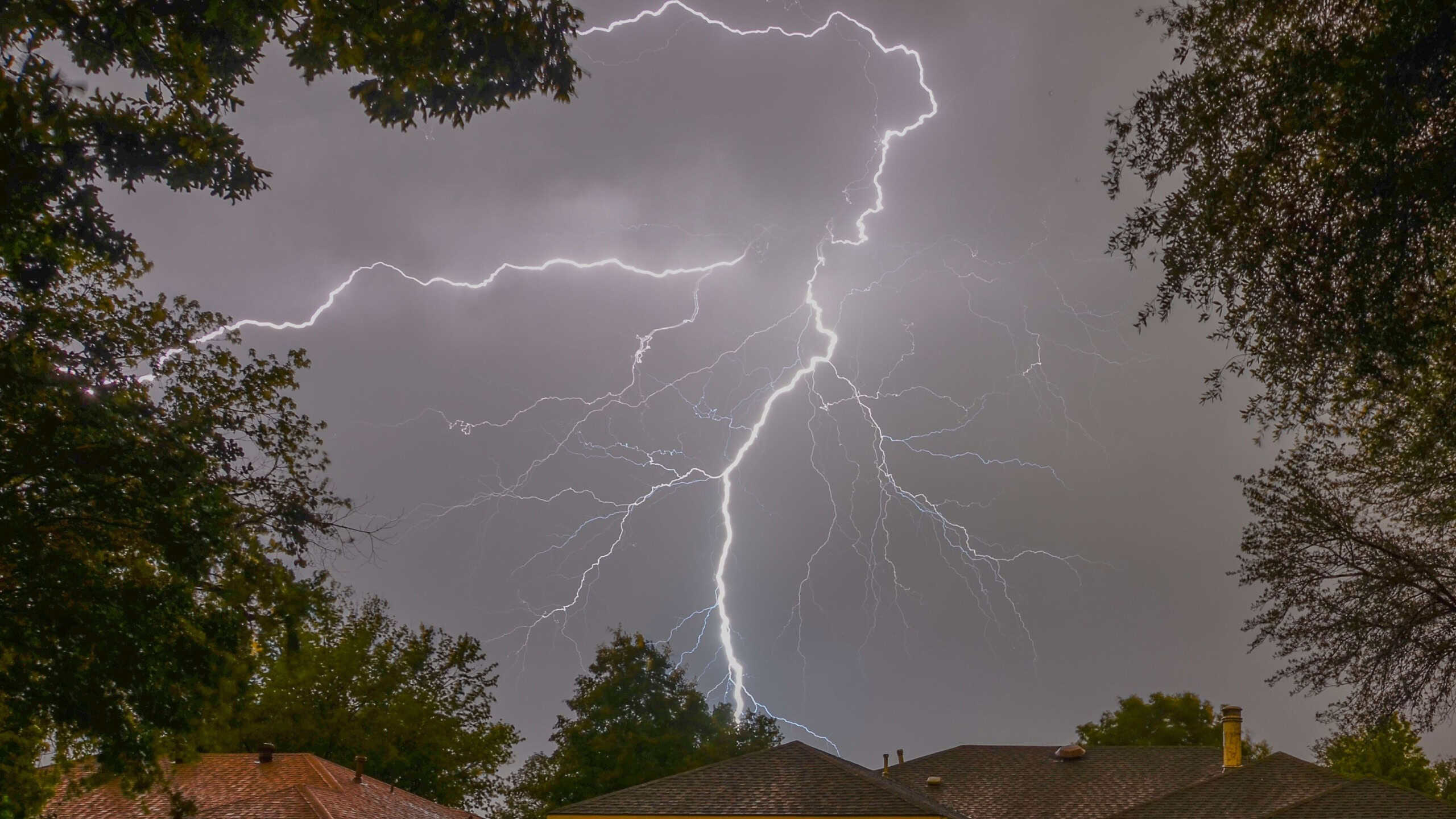 A flash of lightning in the gray sky above the roofs of houses